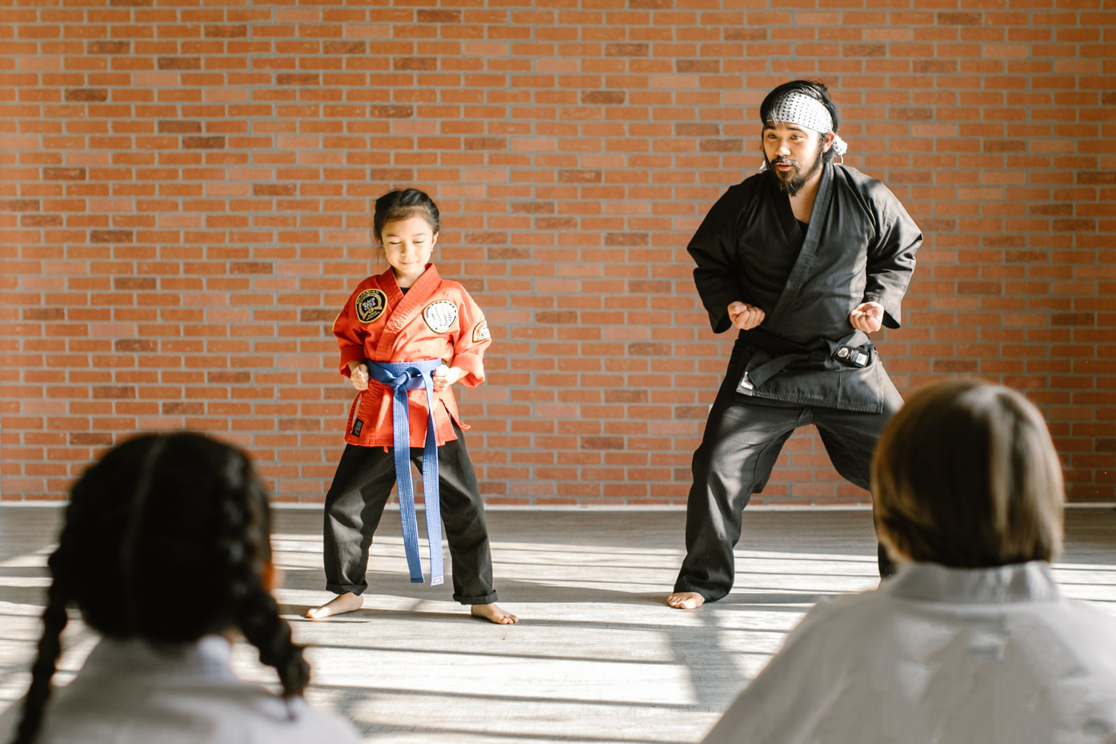 A martial arts instructor and a young student demonstrating a stance in a bright studio.