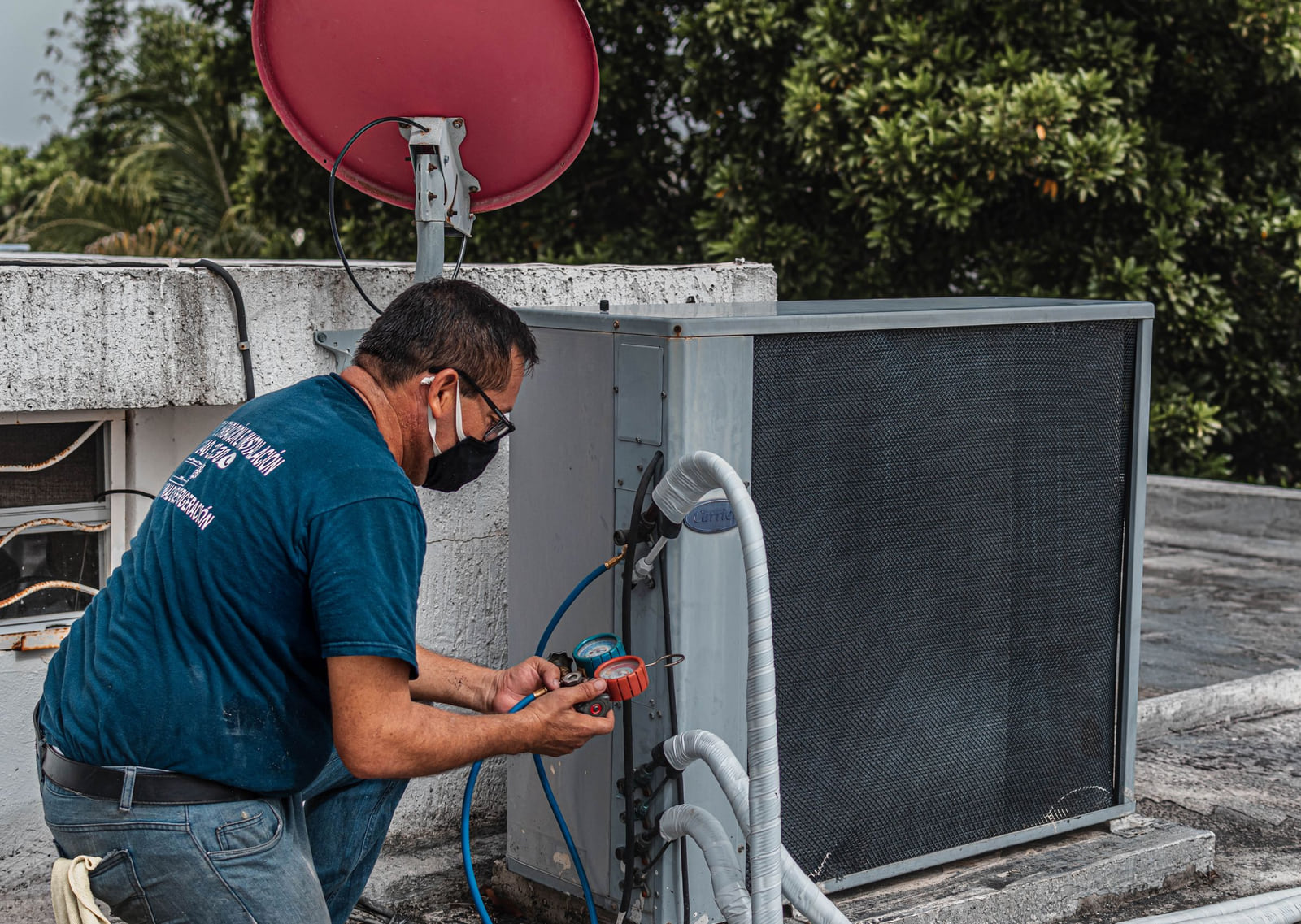 An HVAC technician checking gauges beside an outdoor air-conditioning unit.