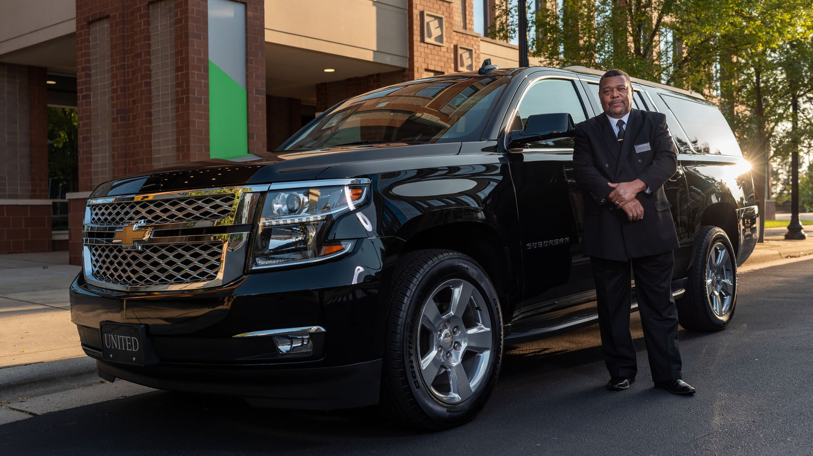 A professionally dressed driver standing beside a polished black SUV.