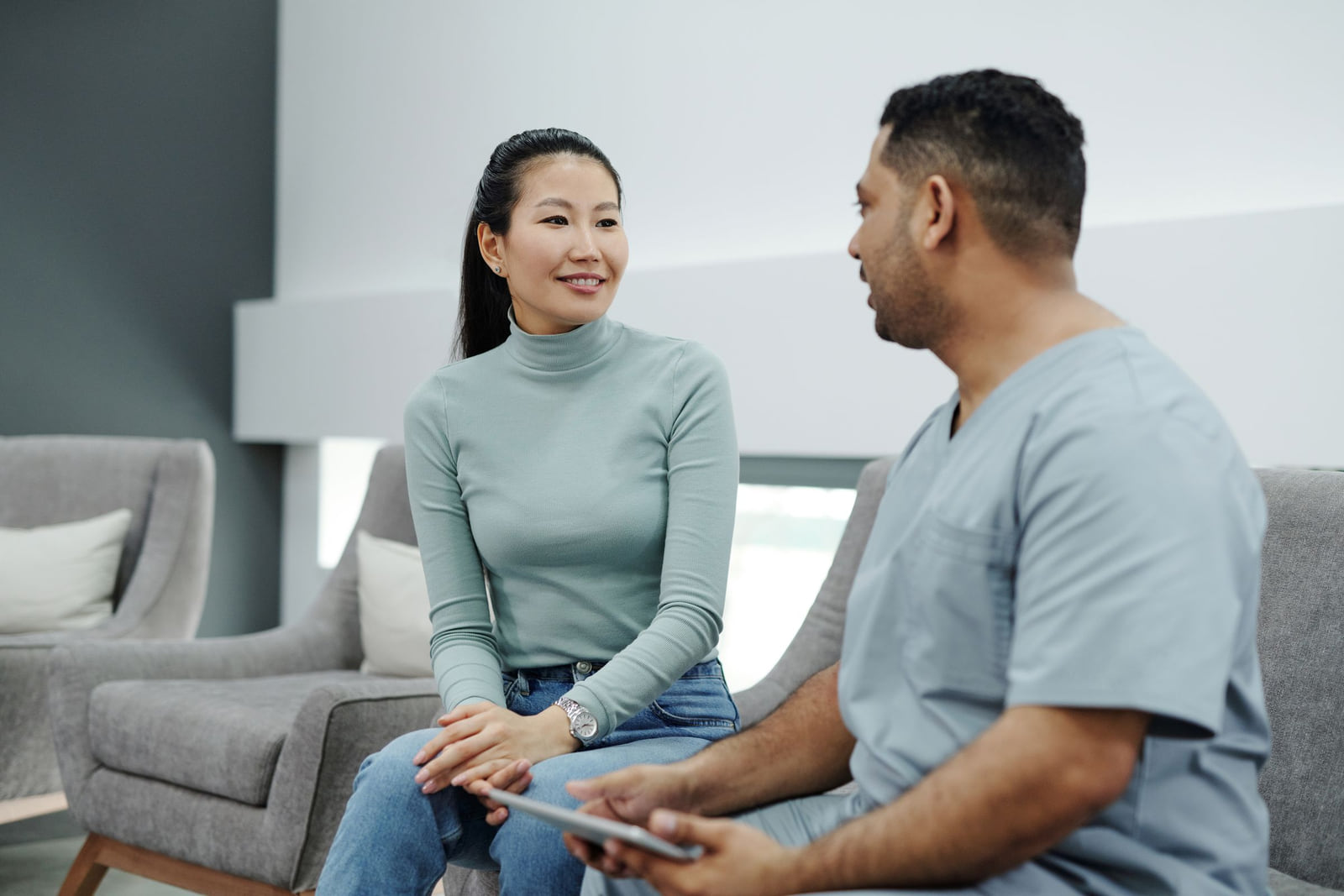 A medical professional talking with a seated patient in a clinic.