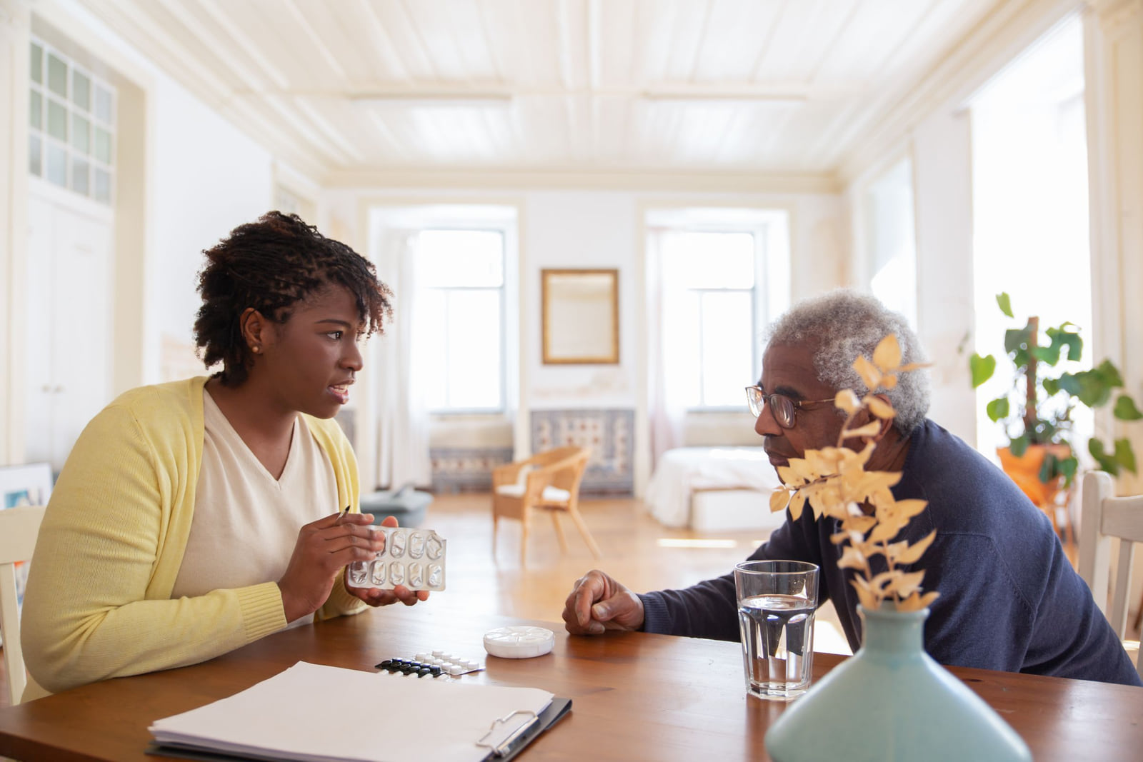 A caregiver discussing medication with an older man across a table.