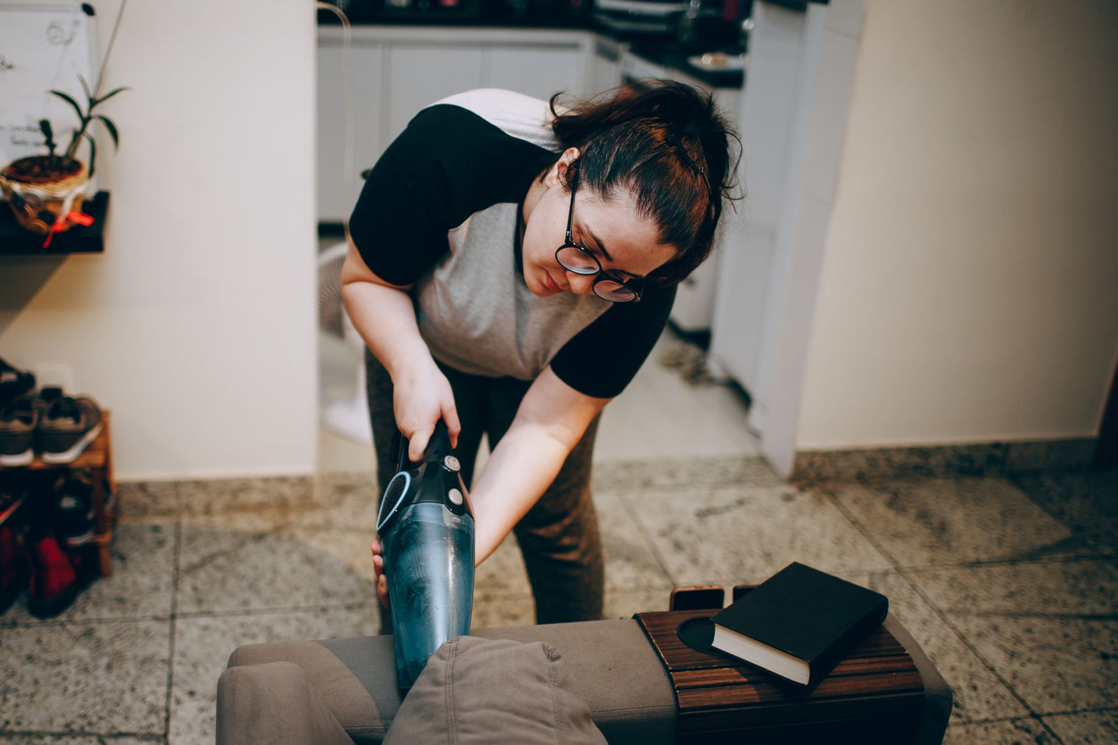 A person vacuuming an upholstered sofa in a living room.