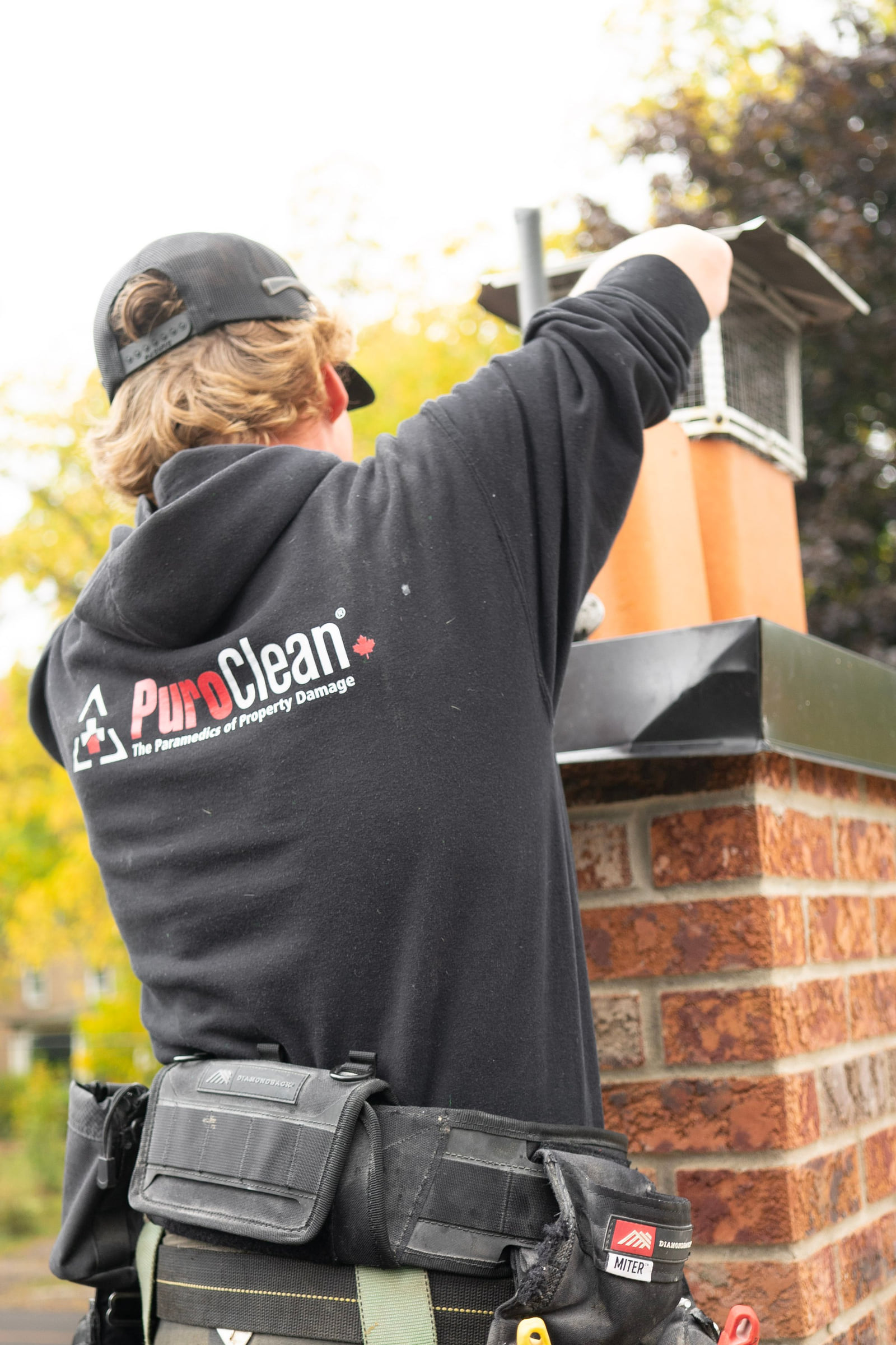 A chimney worker using a long tool beside a brick chimney.