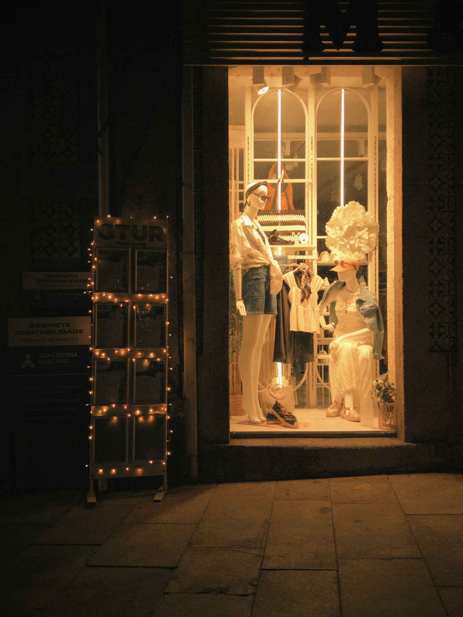 A warmly lit fashion boutique window seen from the street at night.