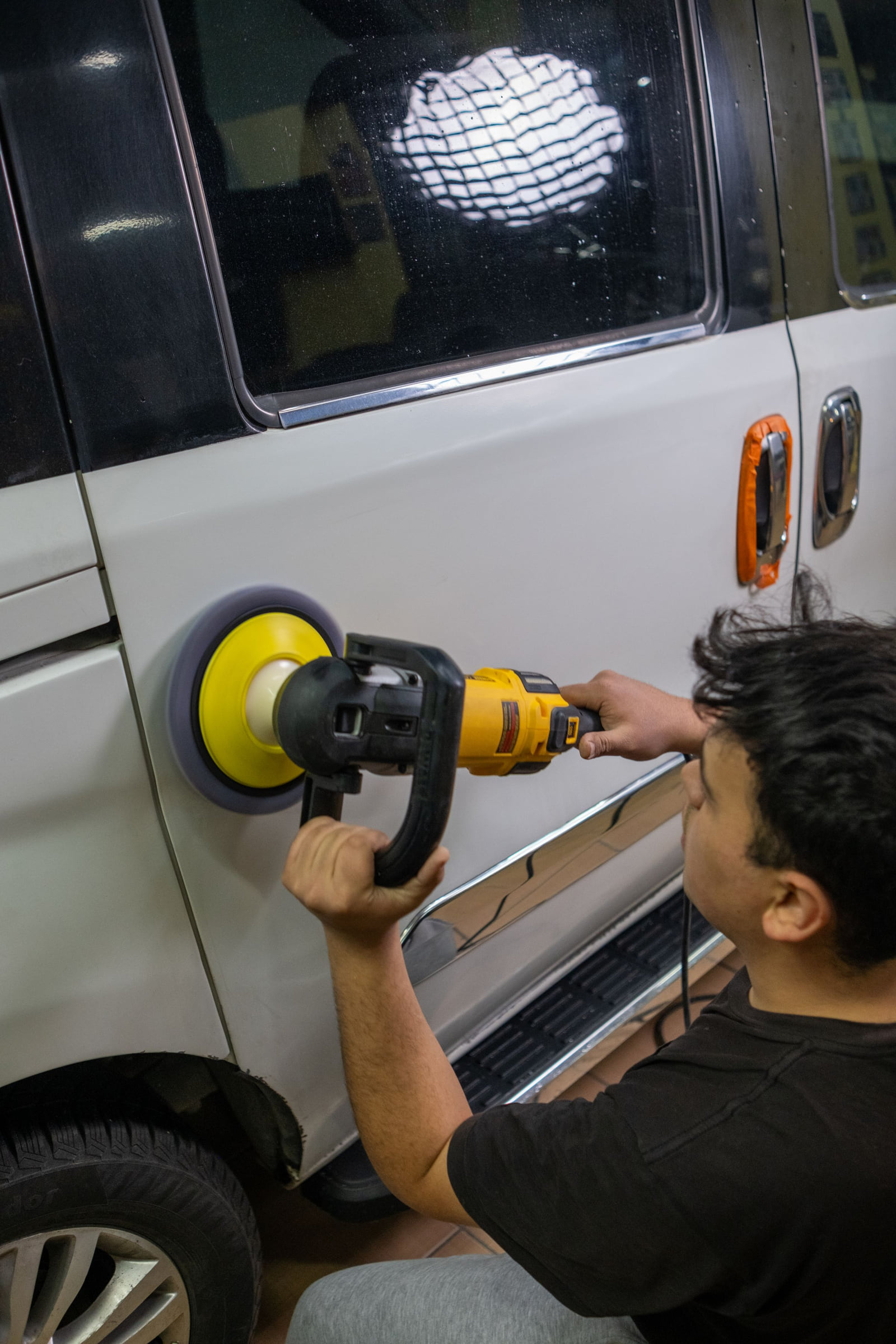 A detailer polishing the side of a van with a powered polishing tool.