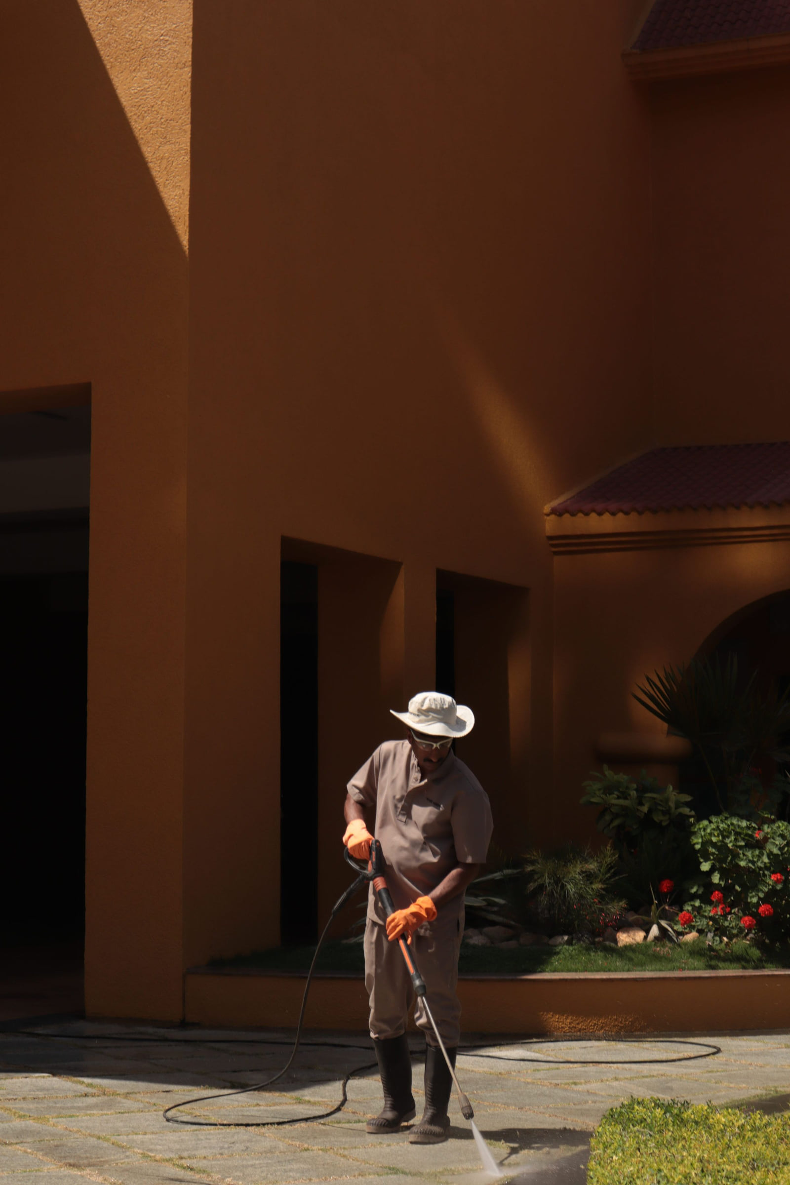 An outdoor worker cleaning pavement with a water hose.