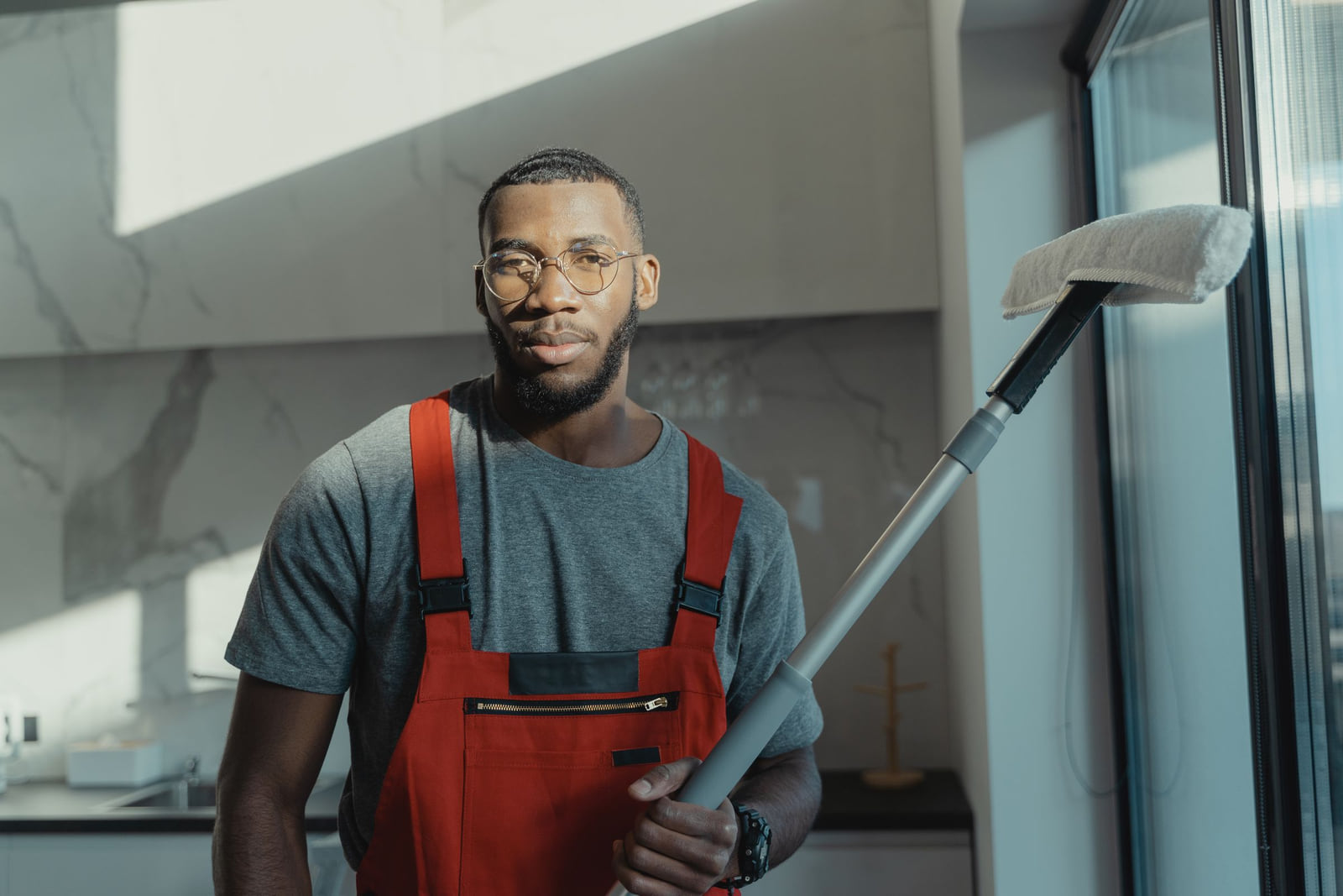 A cleaner in red overalls holding a cleaning tool in a bright interior.