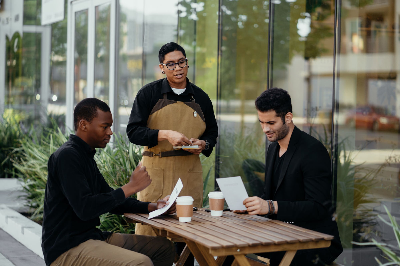 A waiter discussing menus with two customers at an outdoor café table.