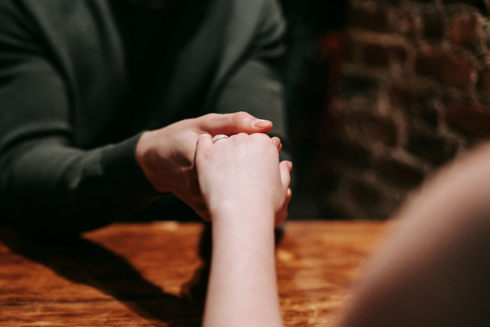 A couple holding hands across a café table with an engagement ring visible.