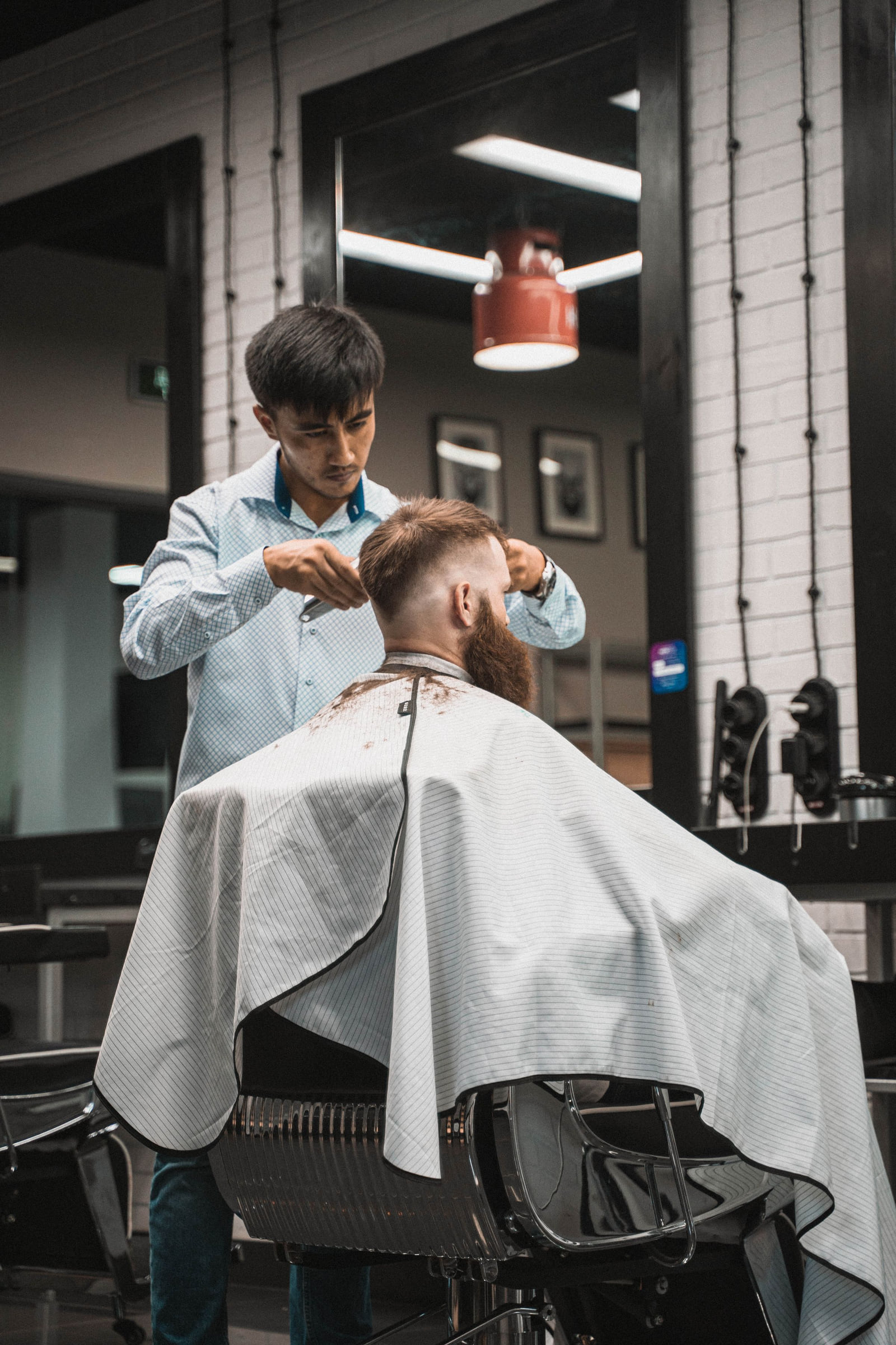 A barber cutting a seated client's hair inside a barbershop.