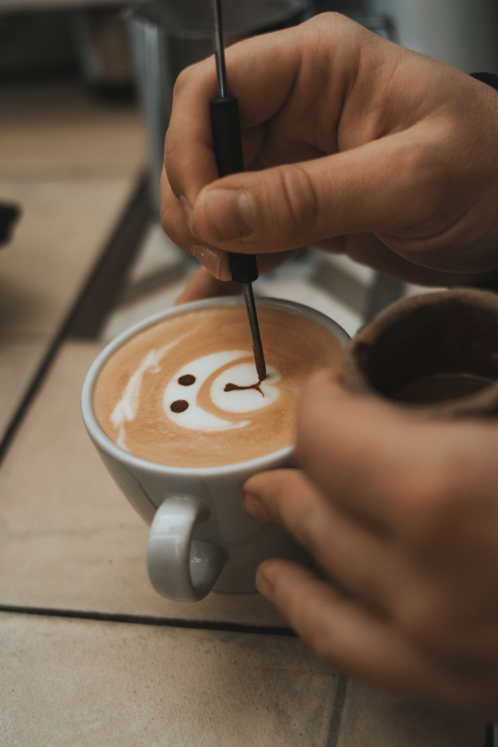 A barista drawing a decorative design in a cup of coffee.
