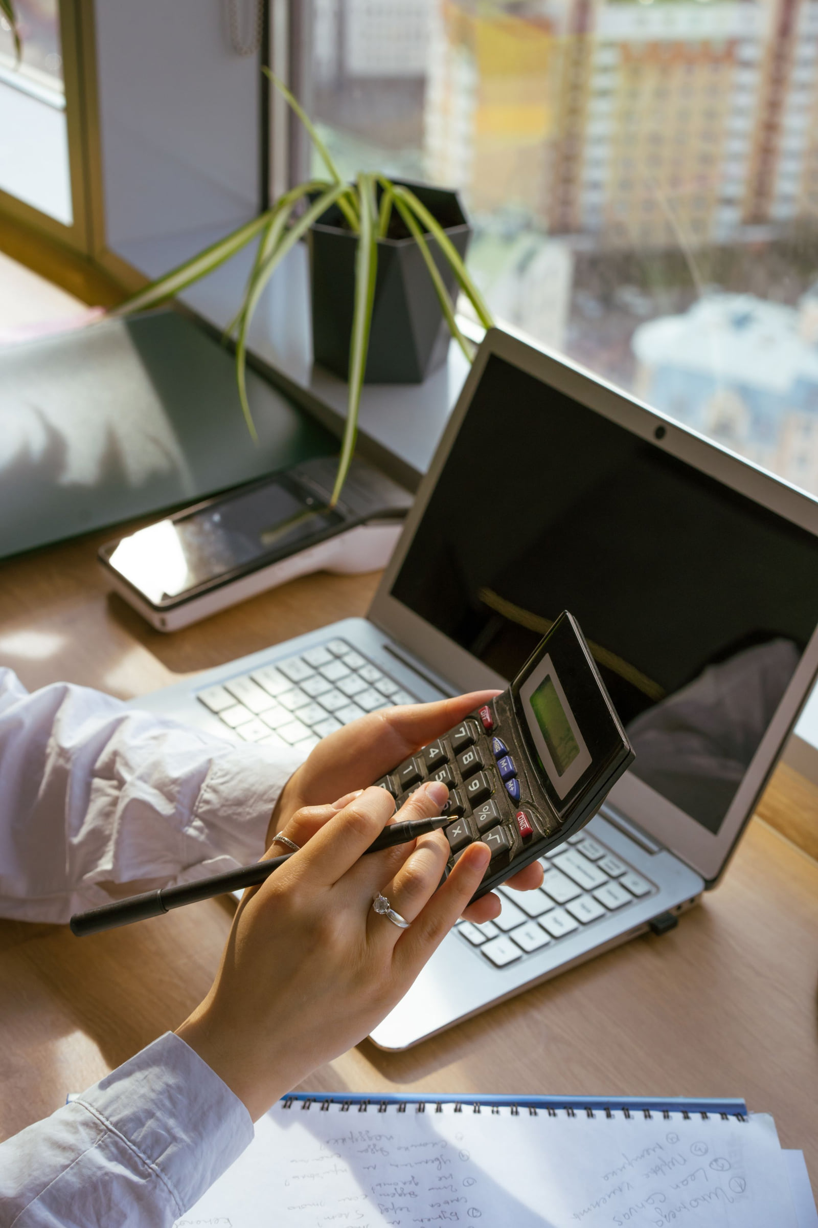 A person using a calculator beside a laptop and financial paperwork.