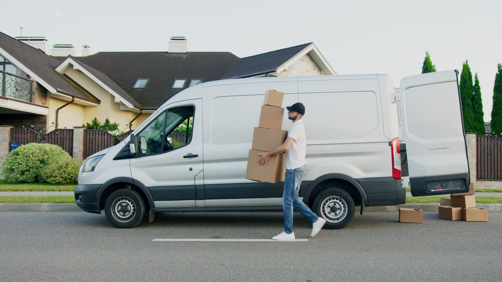 A worker carrying cardboard boxes beside an open white van.