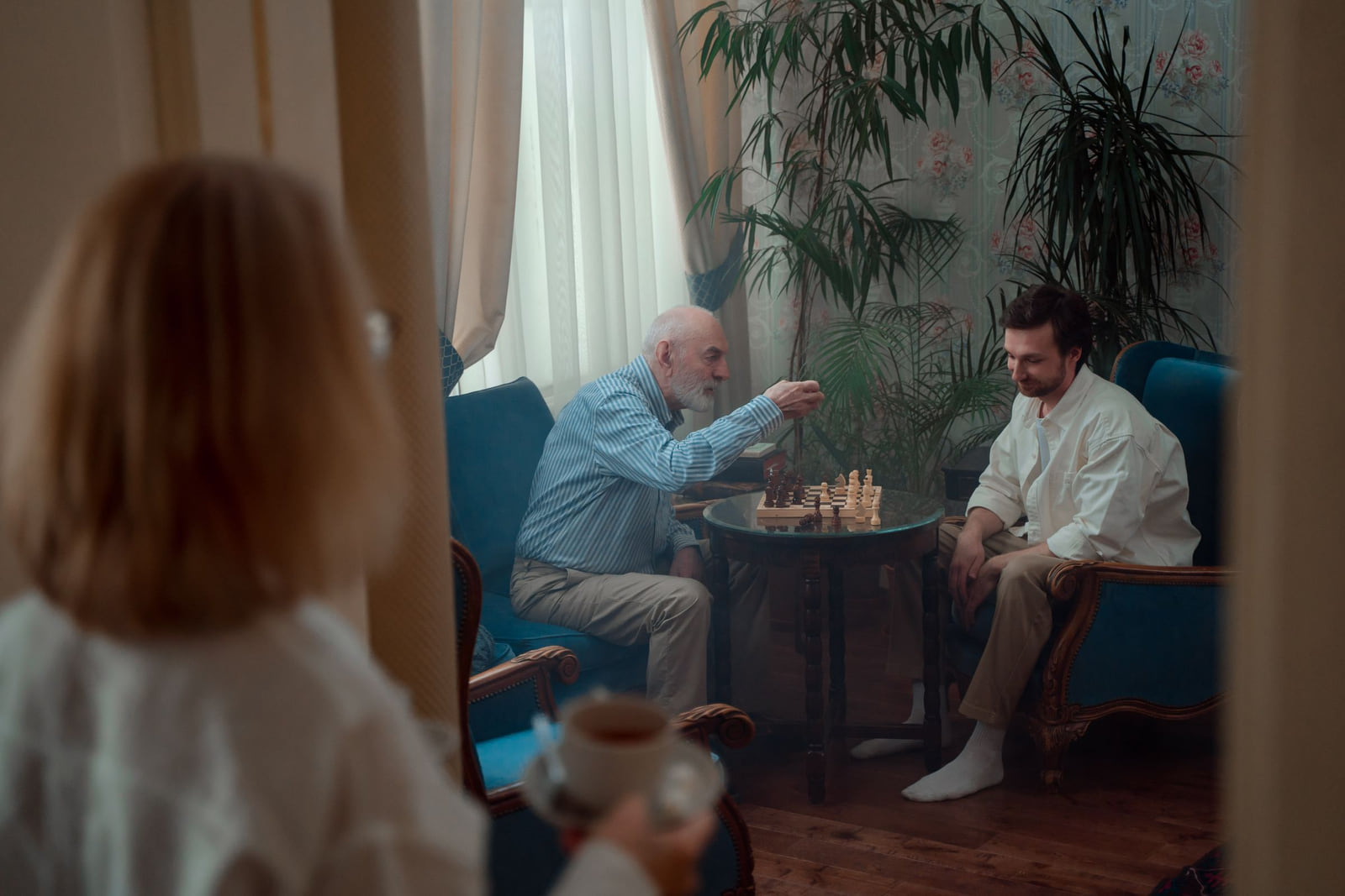 An older man and his adult son playing chess at home.