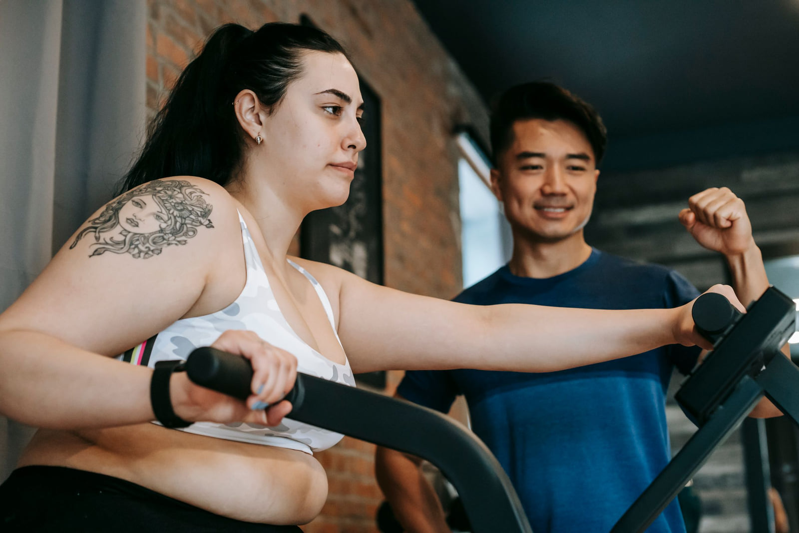 A personal trainer supporting a client on a gym machine.