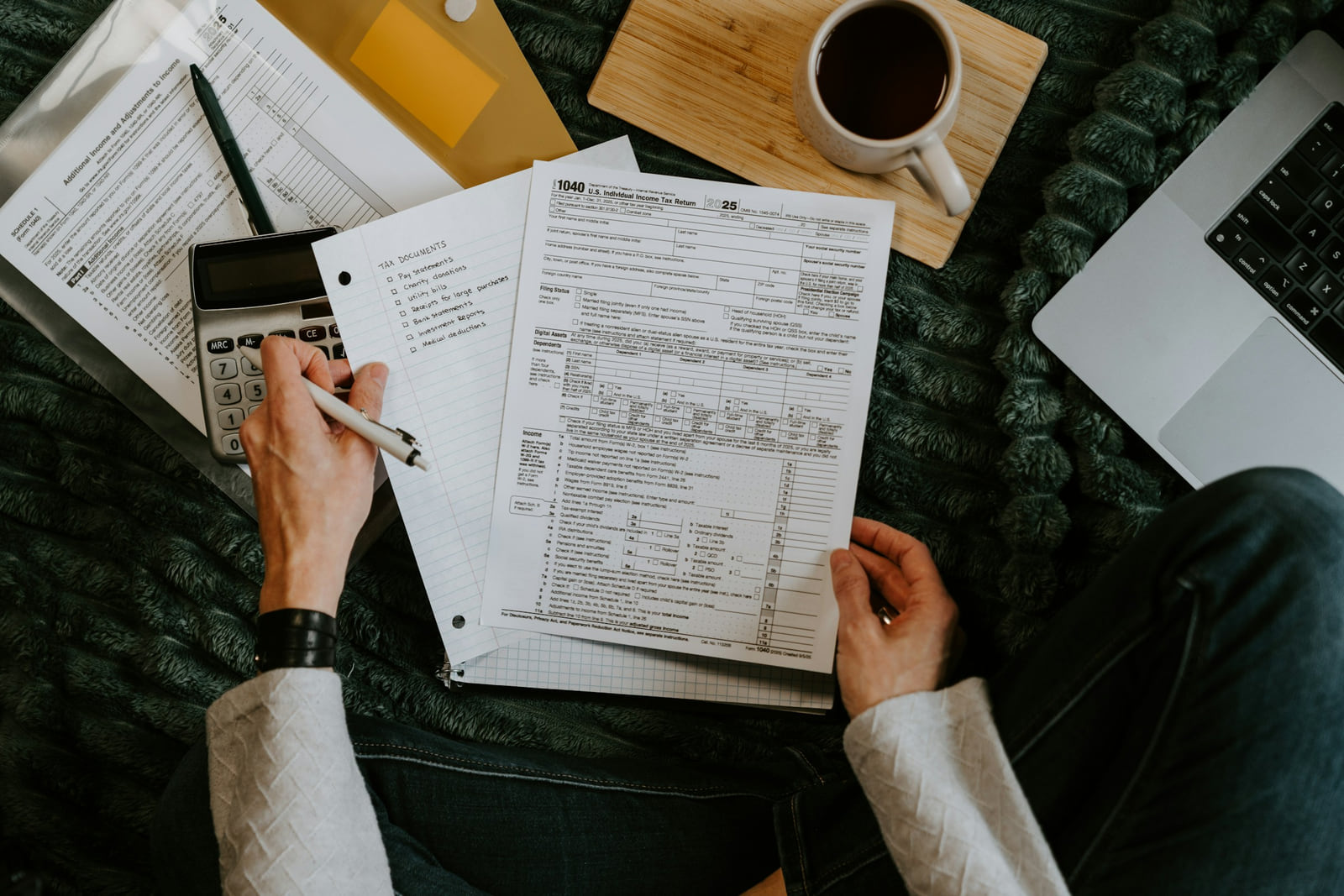 A person reviewing tax forms with a calculator and laptop.