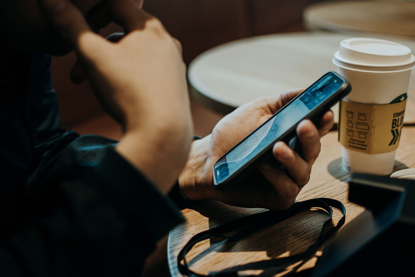 A customer using a smartphone beside a takeaway coffee cup.