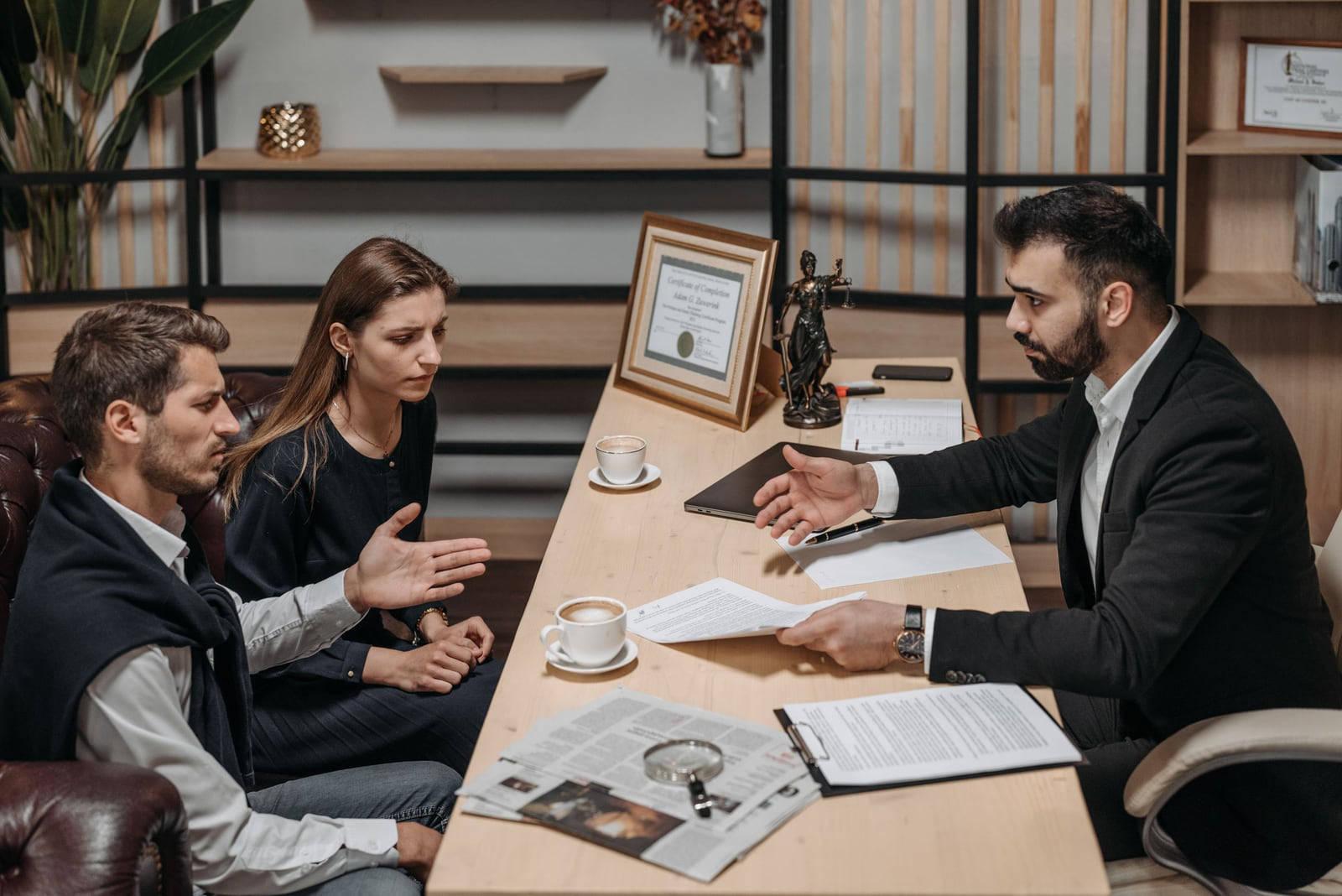 A lawyer discussing documents with two clients across an office desk.