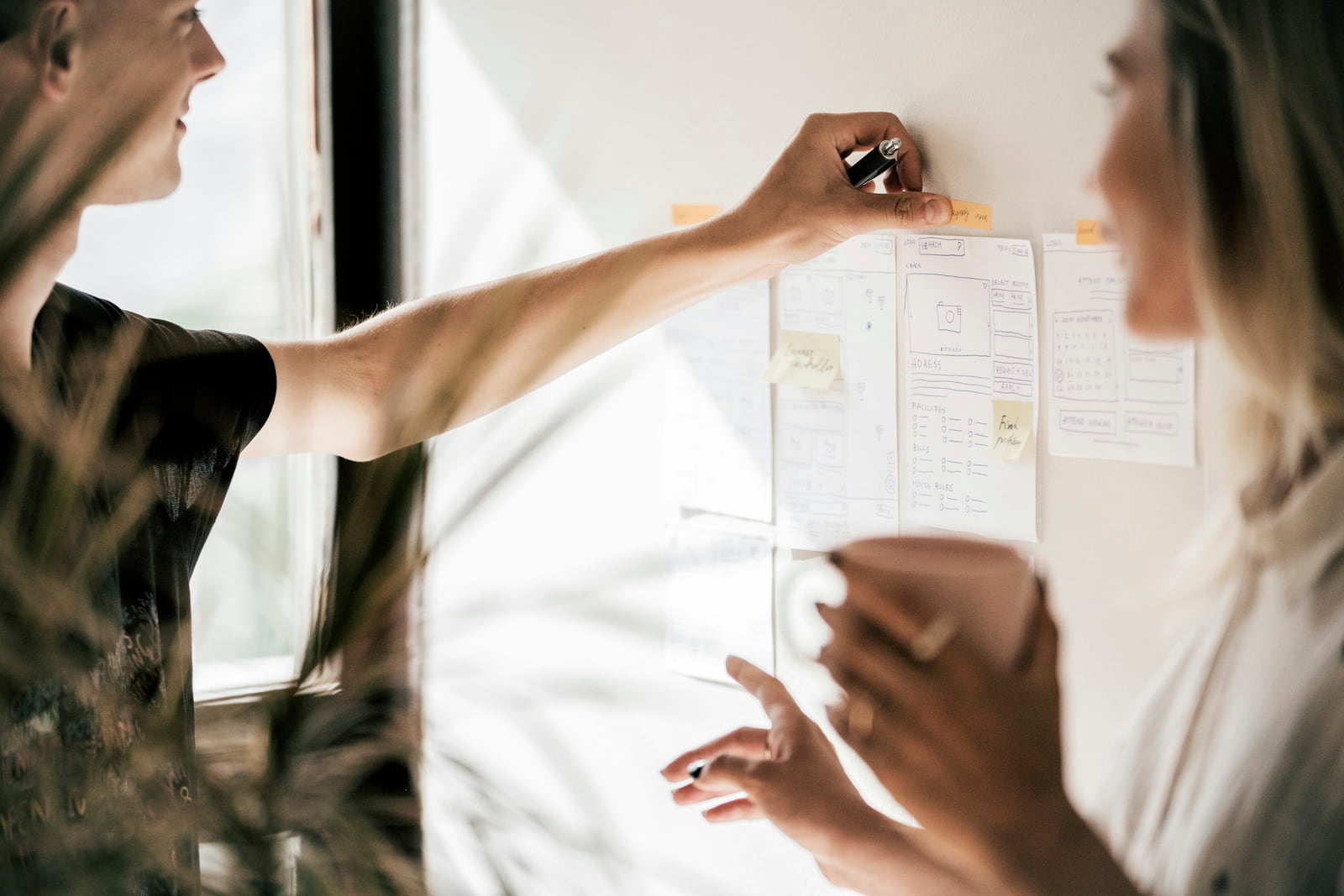 Two people discussing paper website wireframes on a wall.