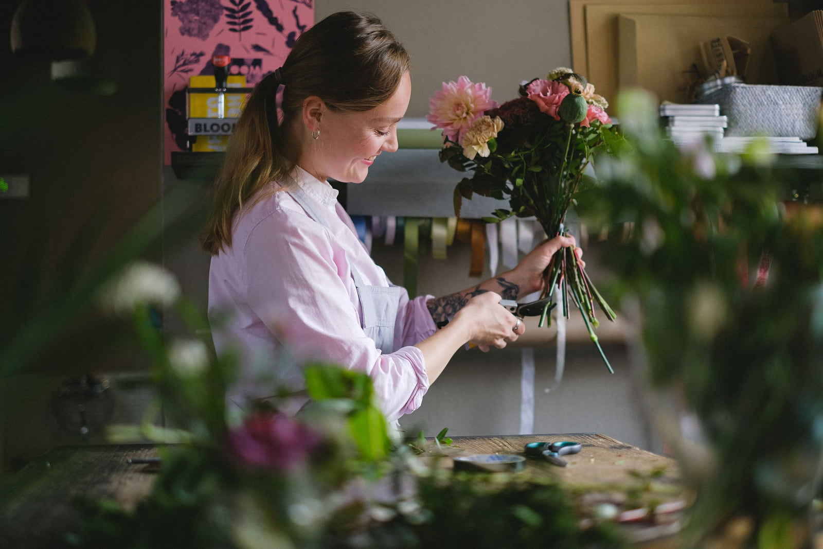 A florist arranging a bouquet at a flower-covered workbench.