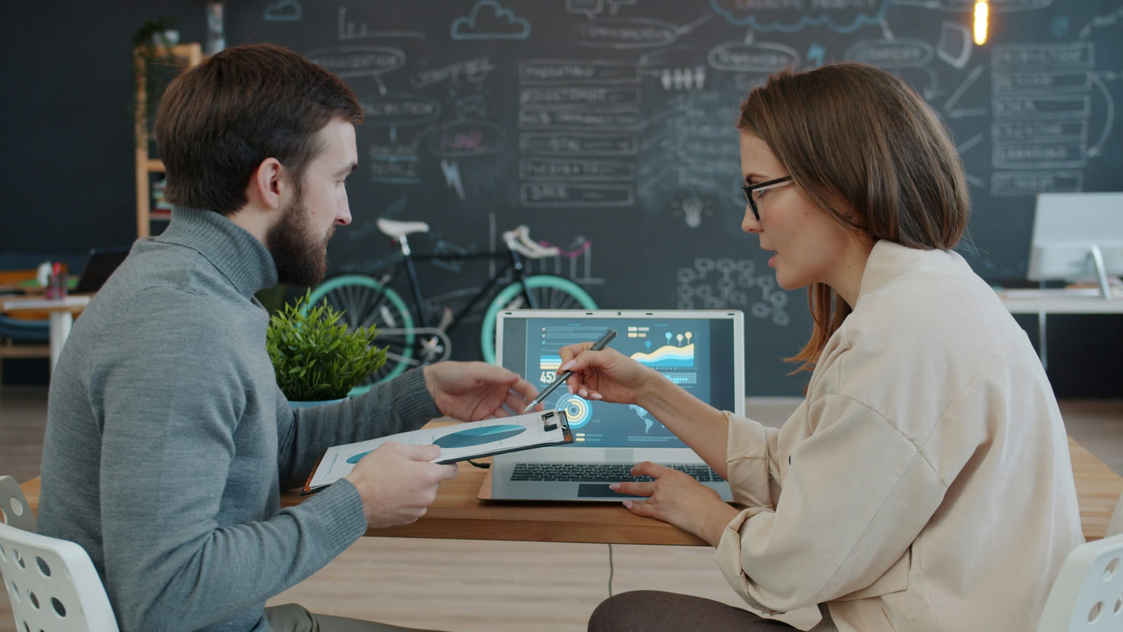Two colleagues reviewing information on a laptop and discussing a document.