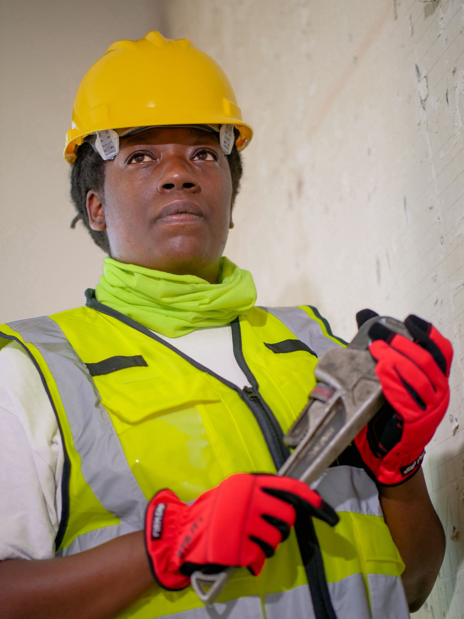 A plumbing worker wearing a hard hat and reflective vest while holding a pipe wrench.