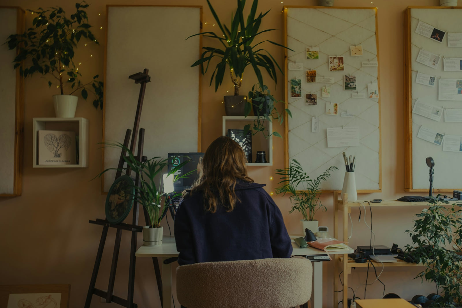 A person updating work at a desk in a light-filled studio with plants.
