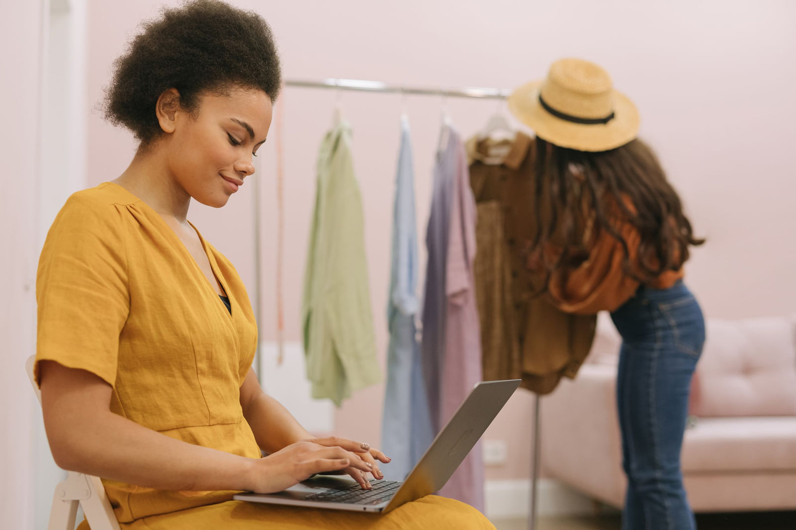 A woman using a laptop in a clothing boutique while a customer browses.