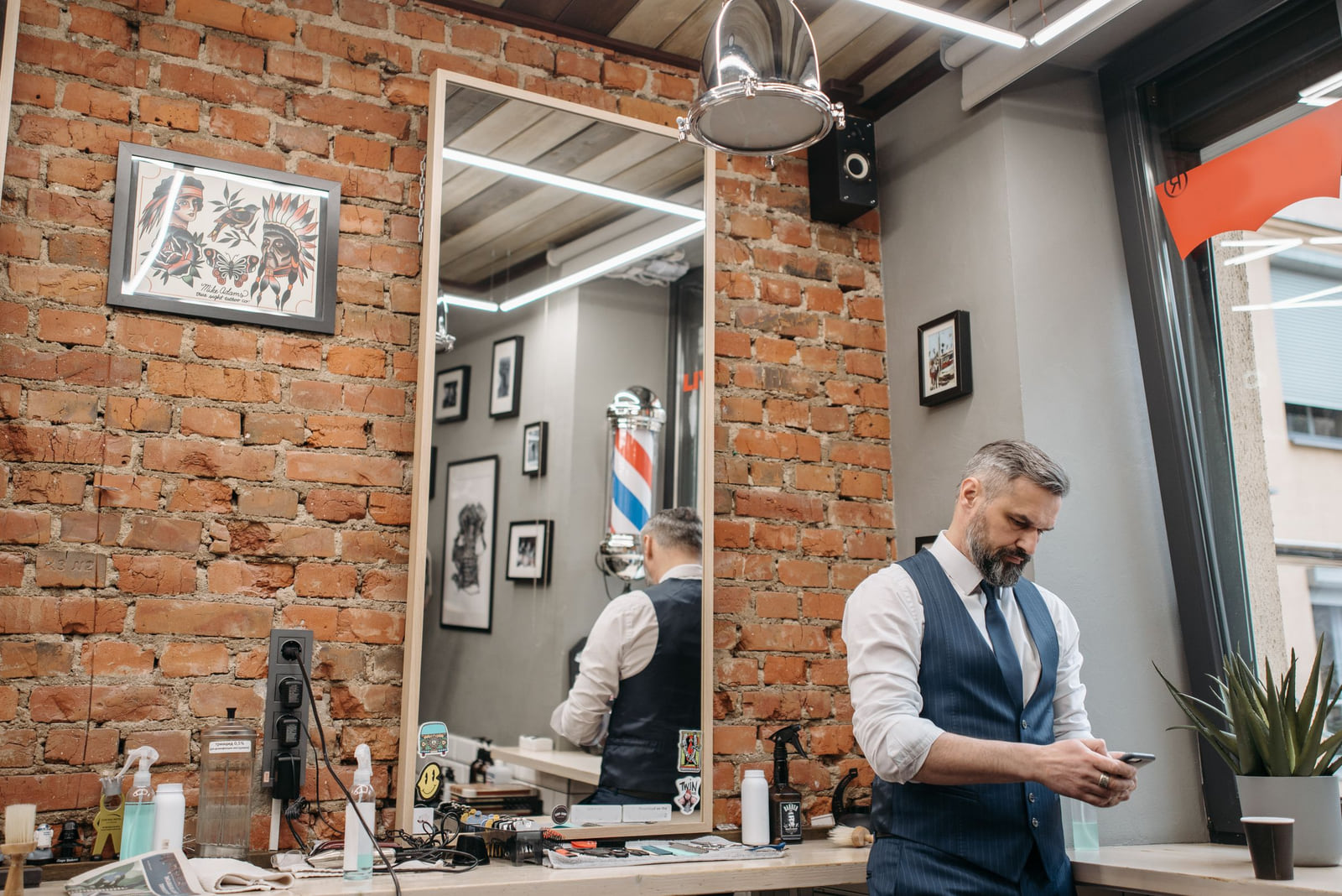 A barber checking a smartphone inside a barbershop.