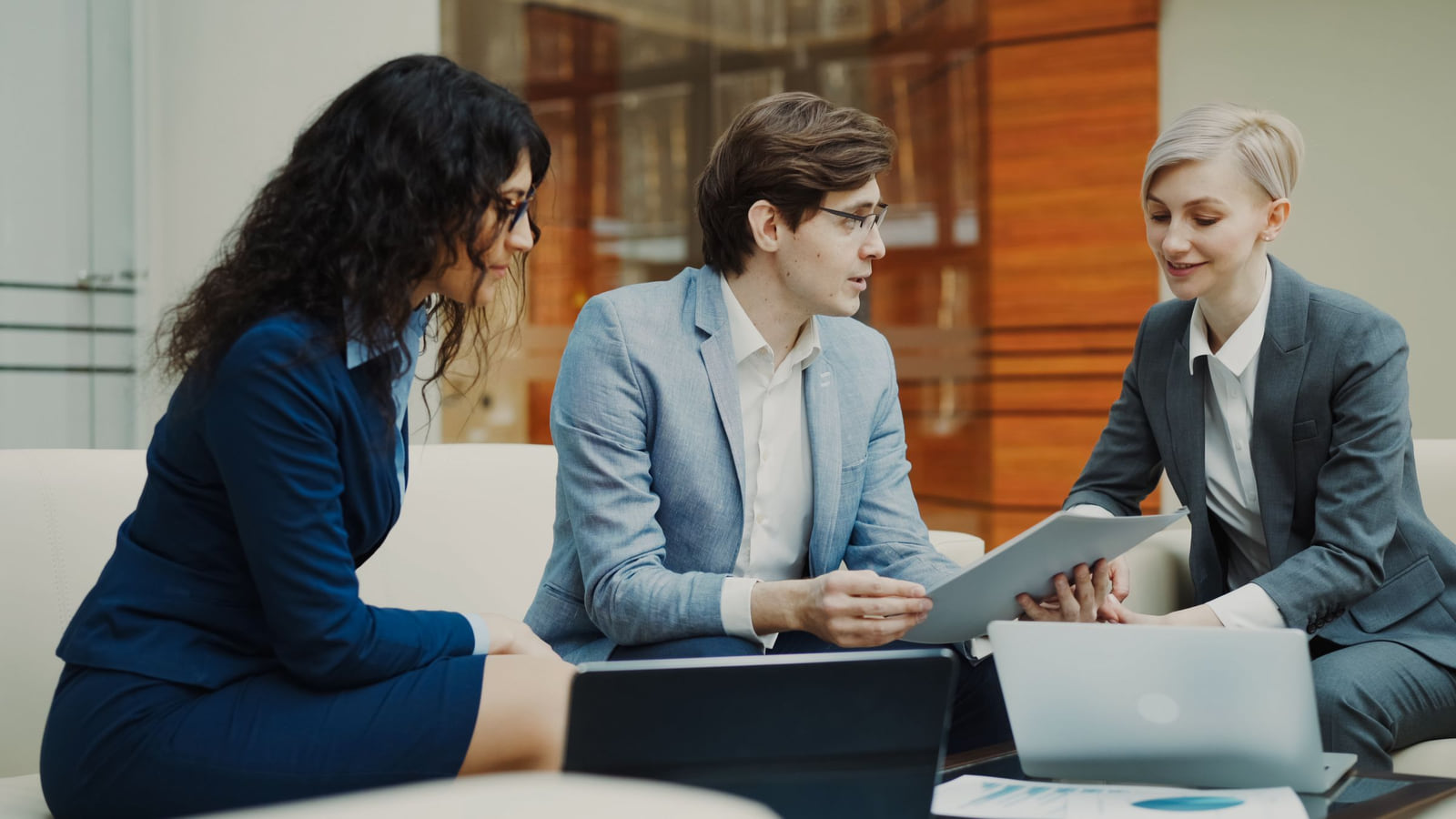 Three colleagues discussing a tablet beside a laptop in an office.