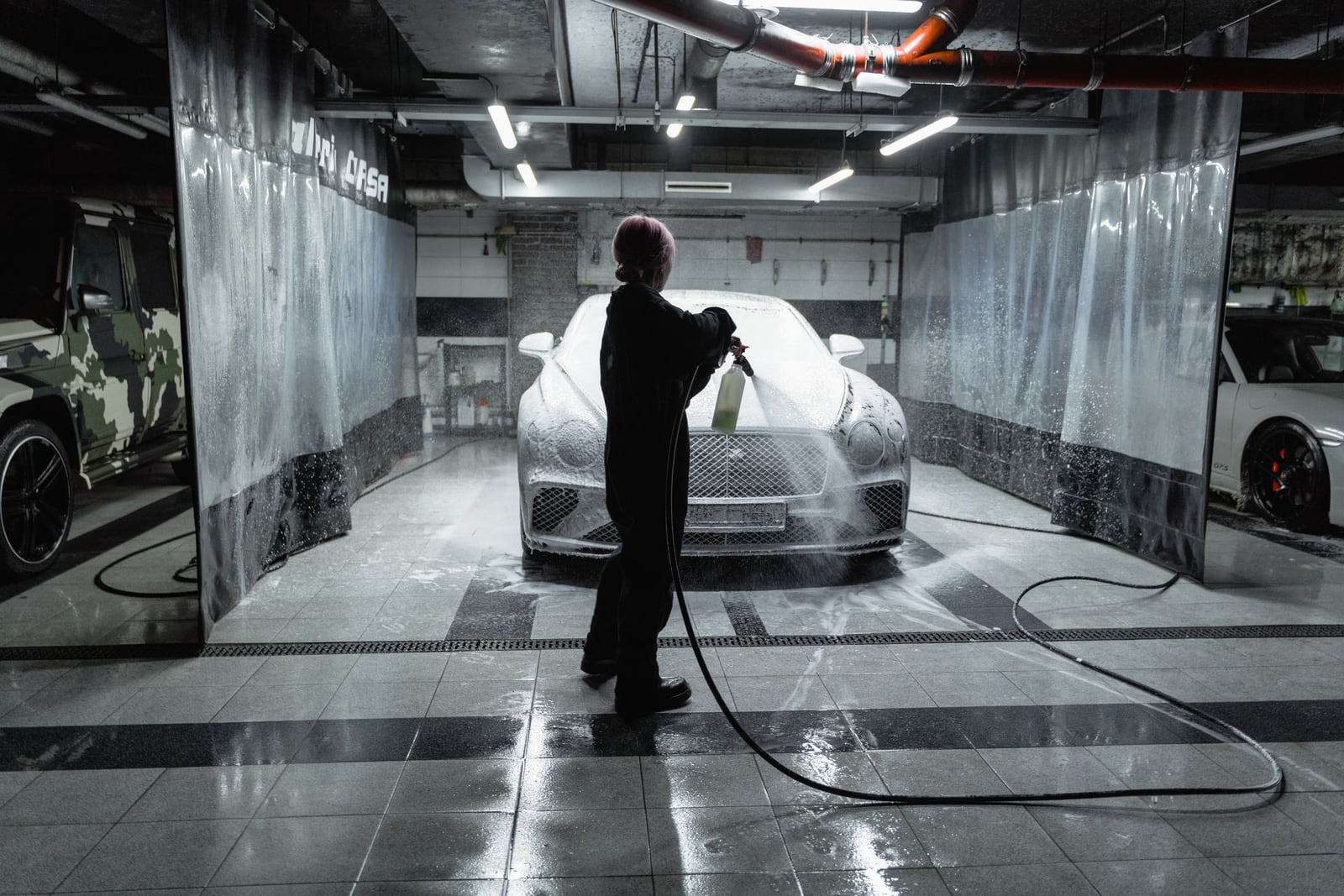 A worker washing a car with a pressure hose in a wash bay.