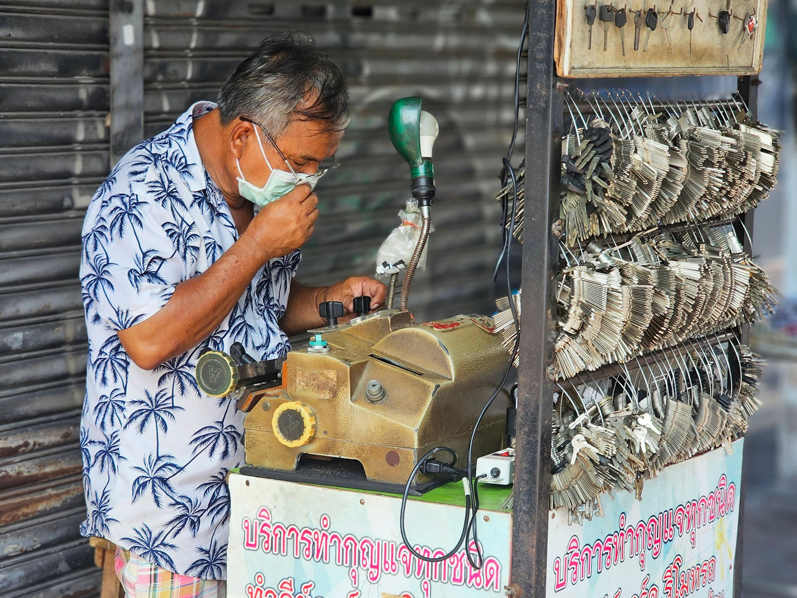 A locksmith working with keys and a key-cutting machine at a street-side counter.