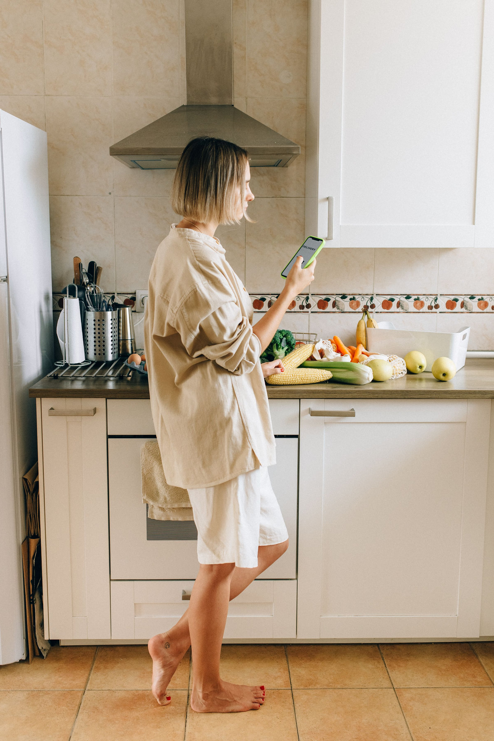 A woman checking a phone while standing at a kitchen counter.