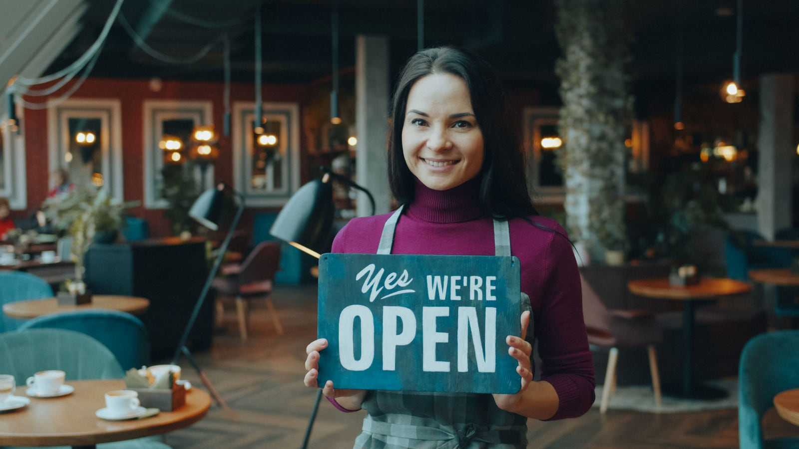 A smiling café owner holding a Yes We're Open sign.