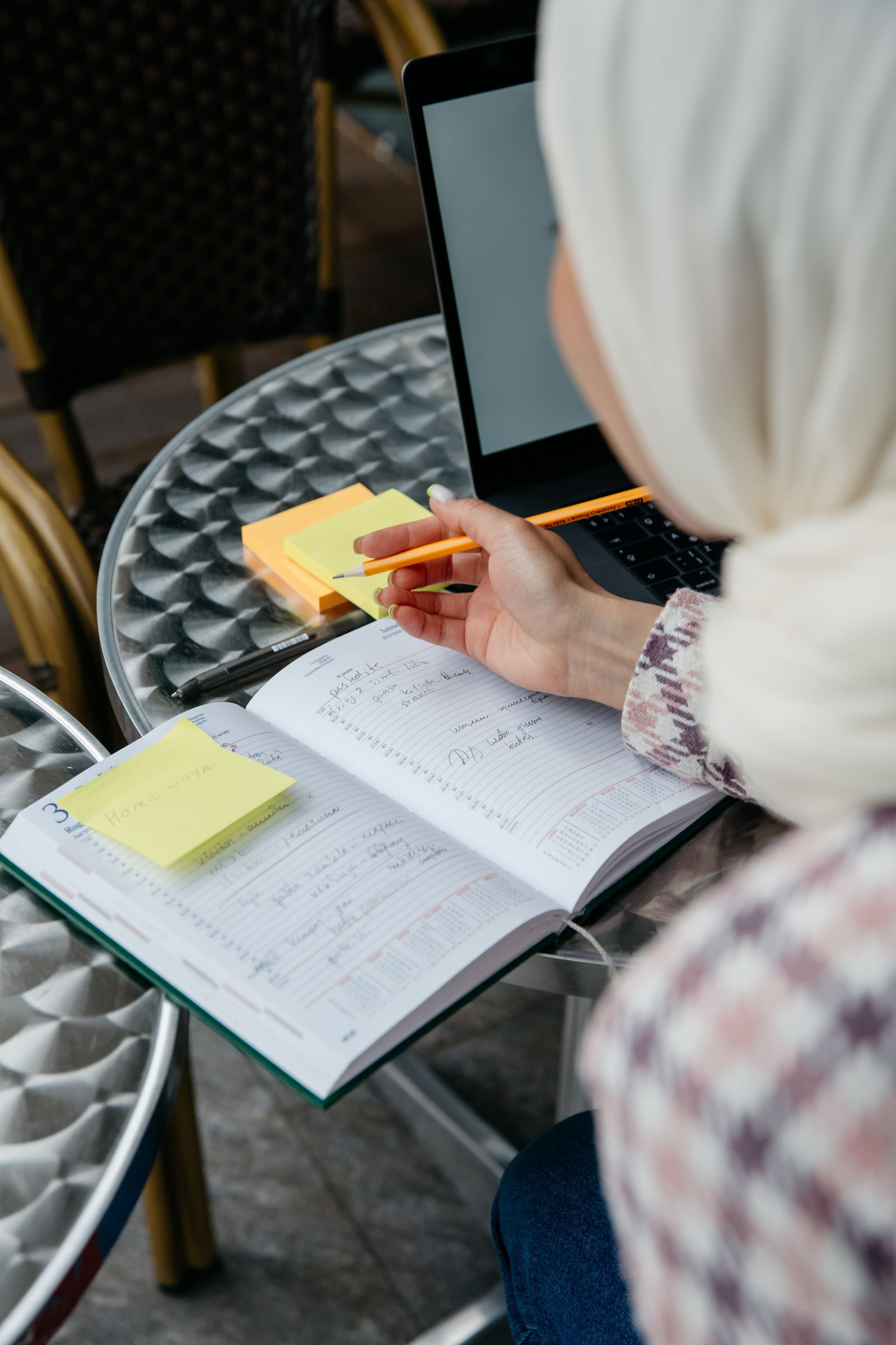 A person writing notes beside a laptop at a café table.