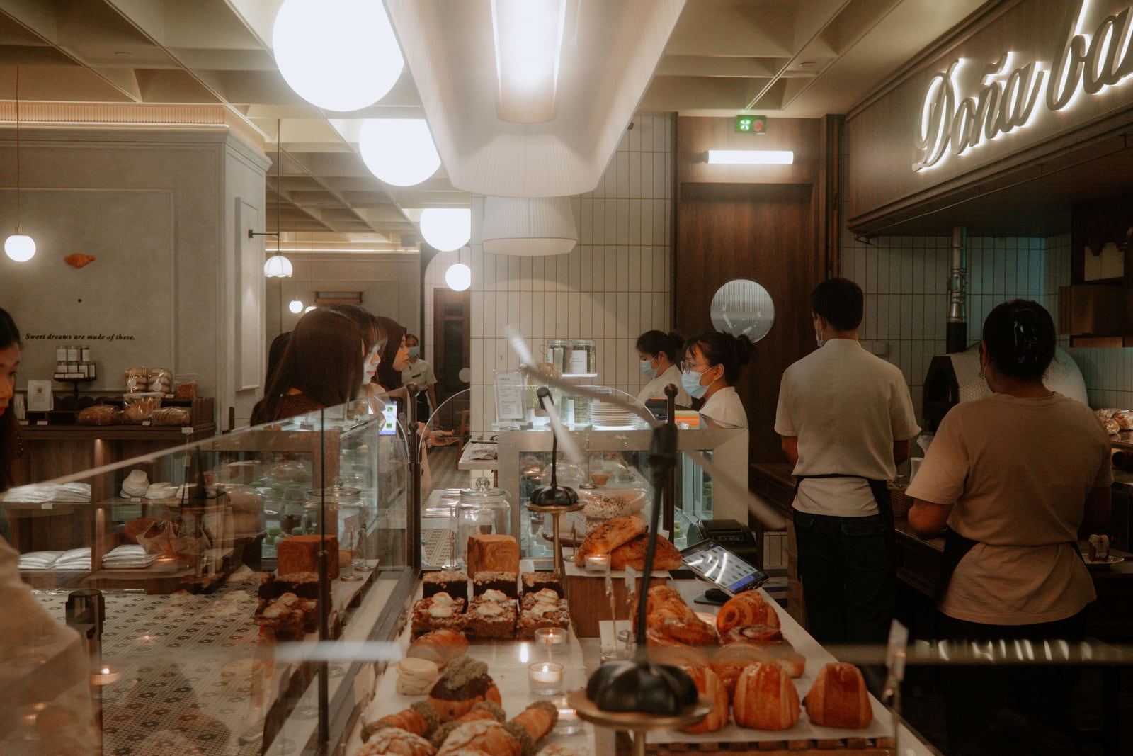 Customers and staff gathered around a bakery's pastry counter.