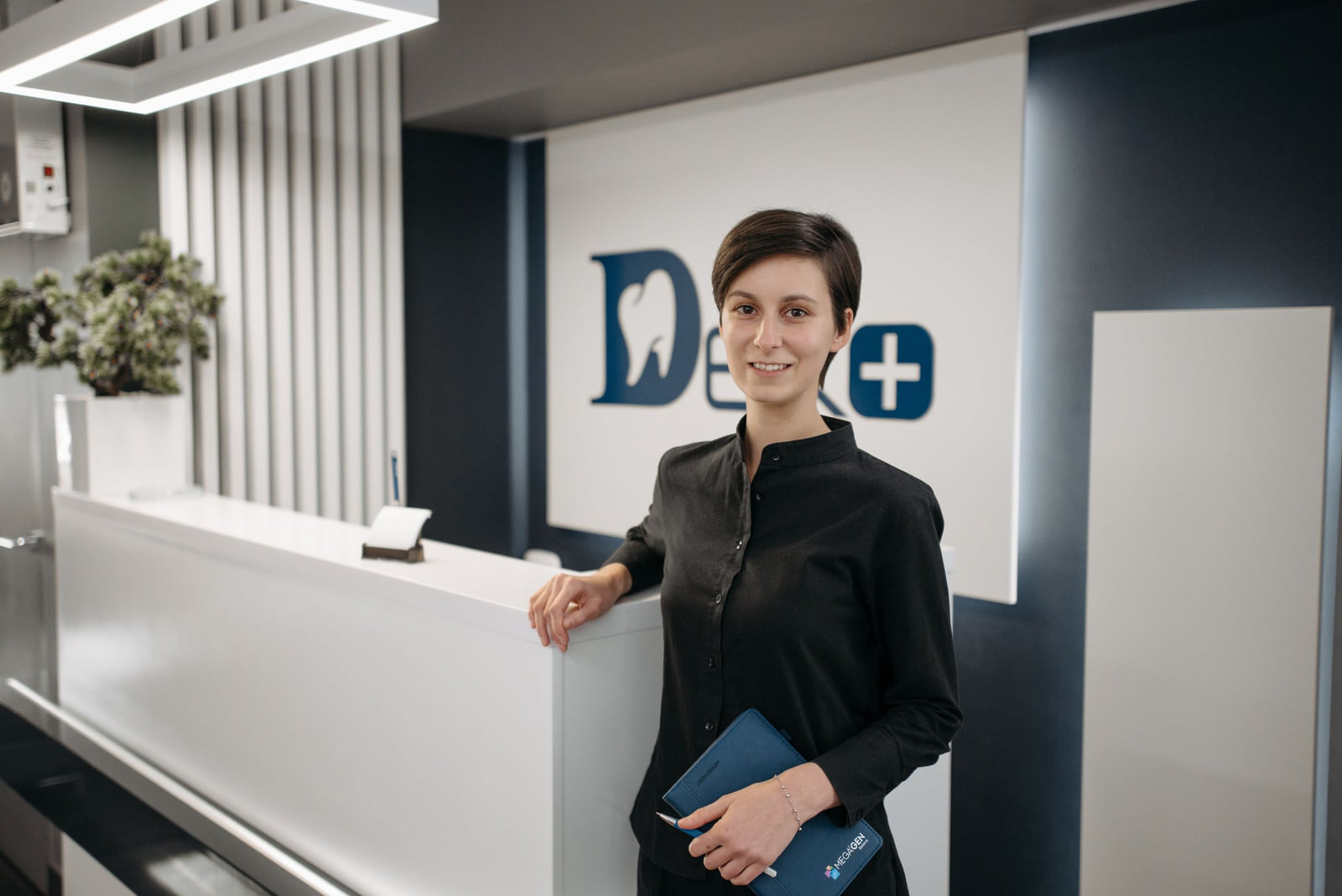 A welcoming staff member at a modern dental reception desk.