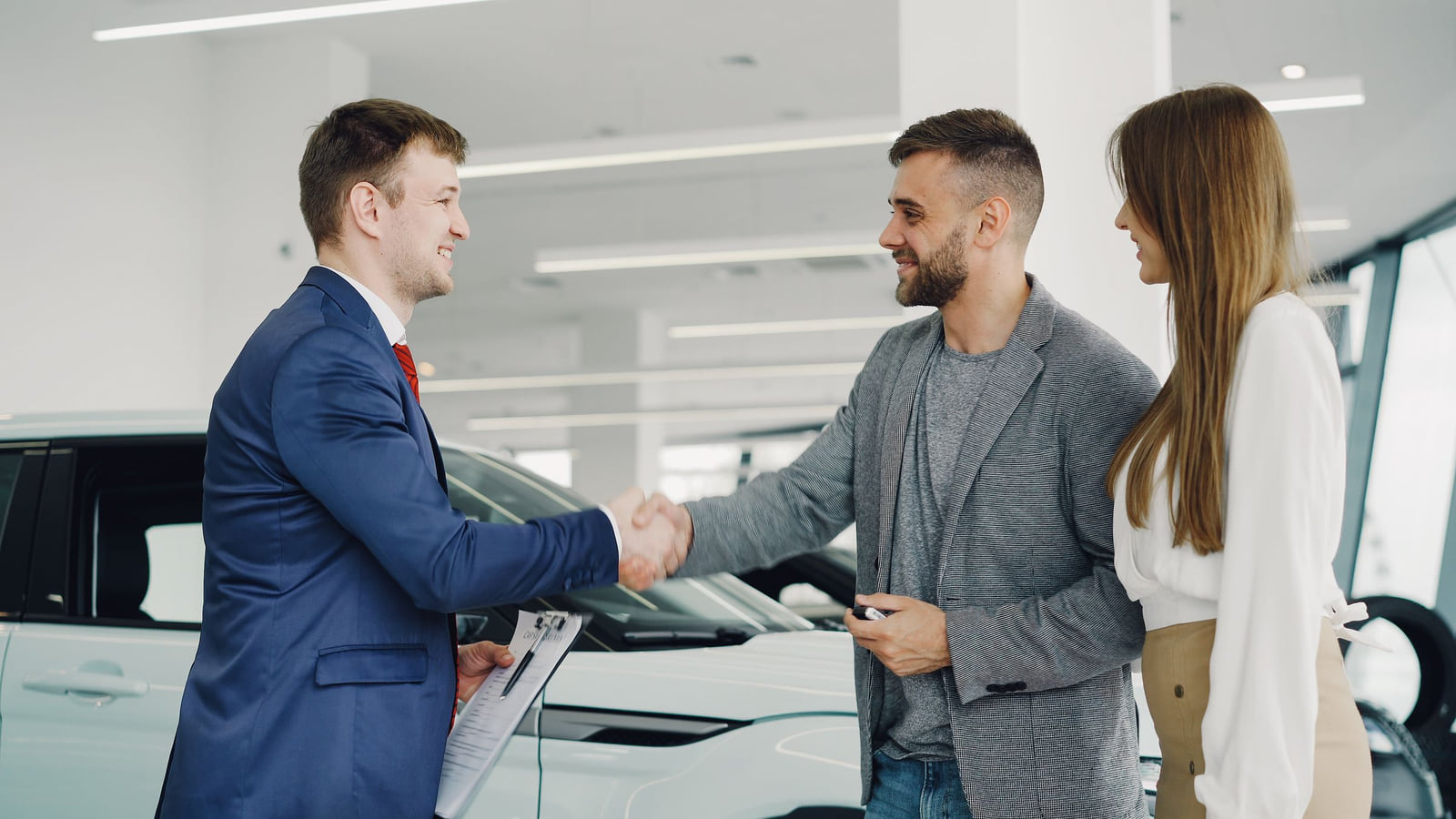 A salesperson shaking hands with a customer in a car showroom.