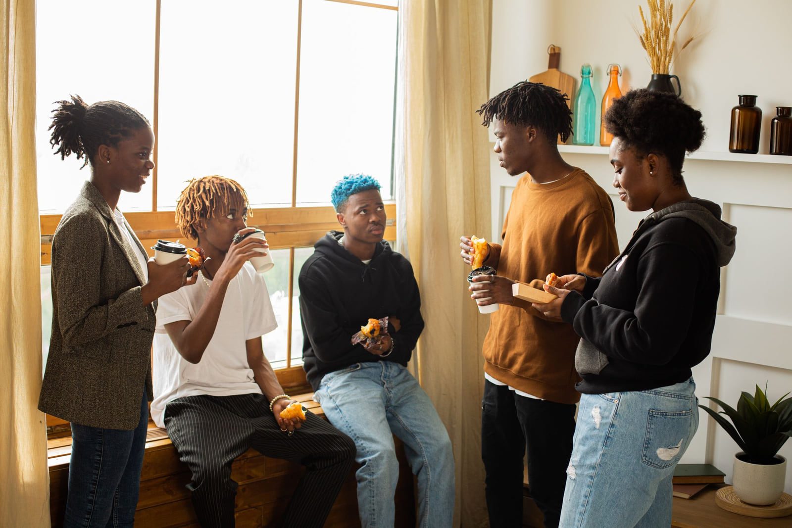A group of friends chatting and eating snacks in a sunny room.