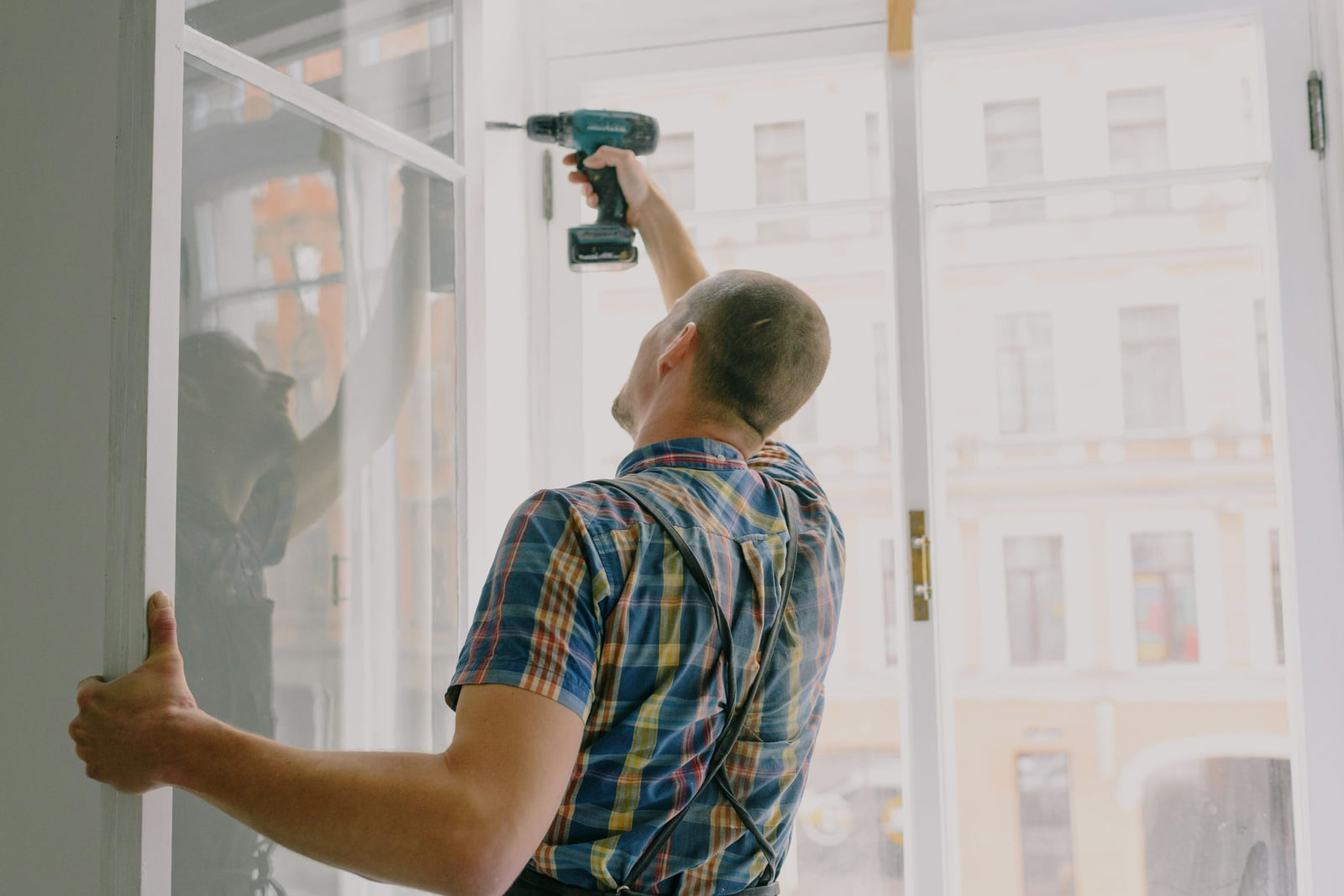 A worker installing a window frame with a drill.