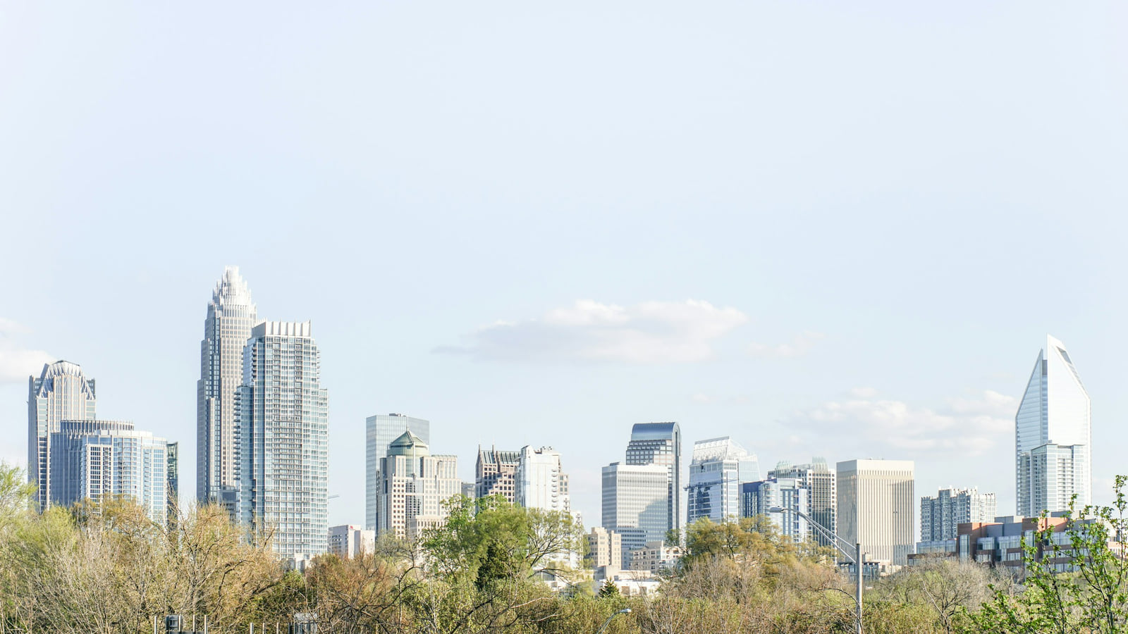 Charlotte's skyline and trees beneath a bright sky.