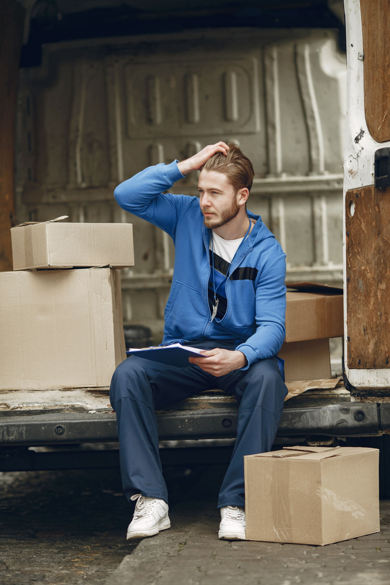 A delivery worker sitting beside parcels at the open back of a van.