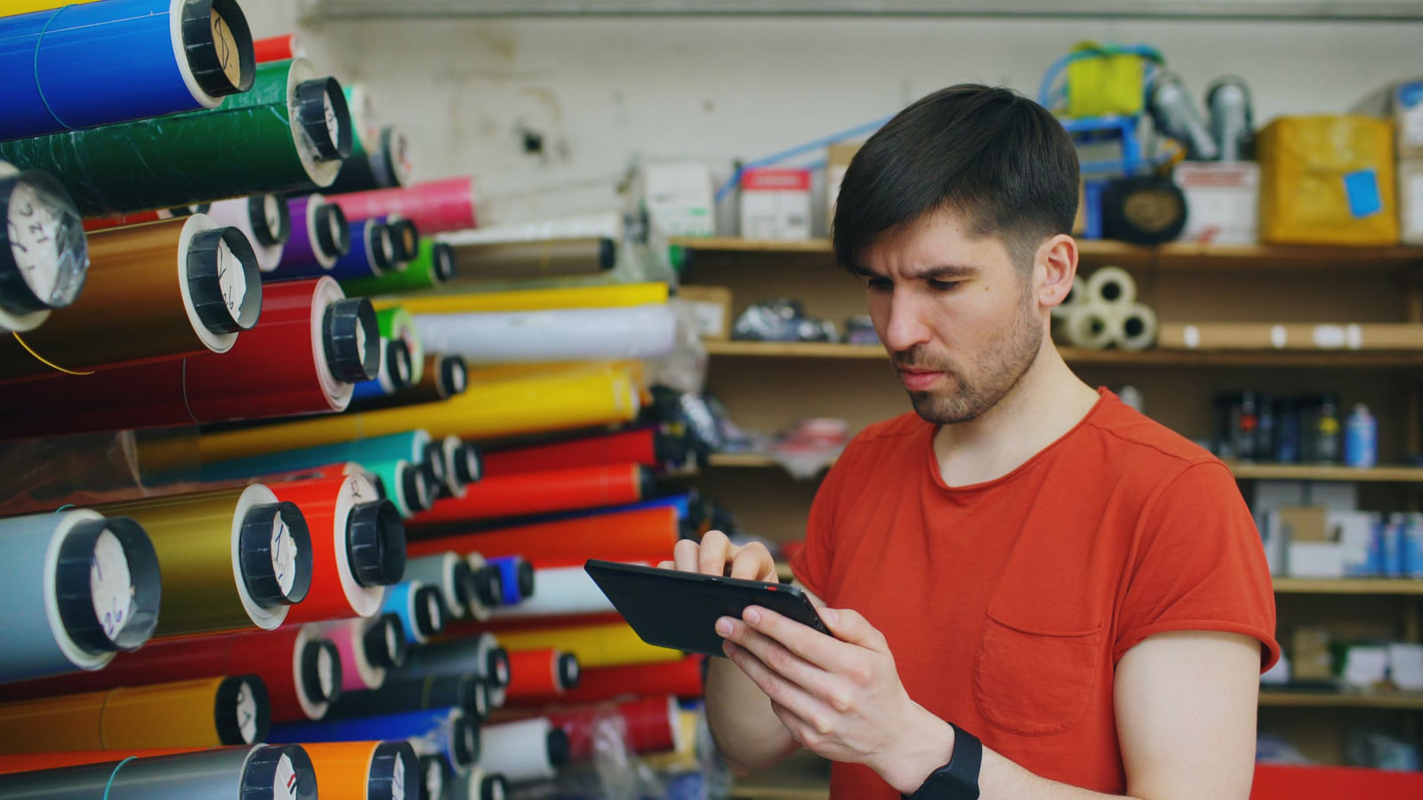 A print-shop worker using a digital tablet beside colorful material rolls.