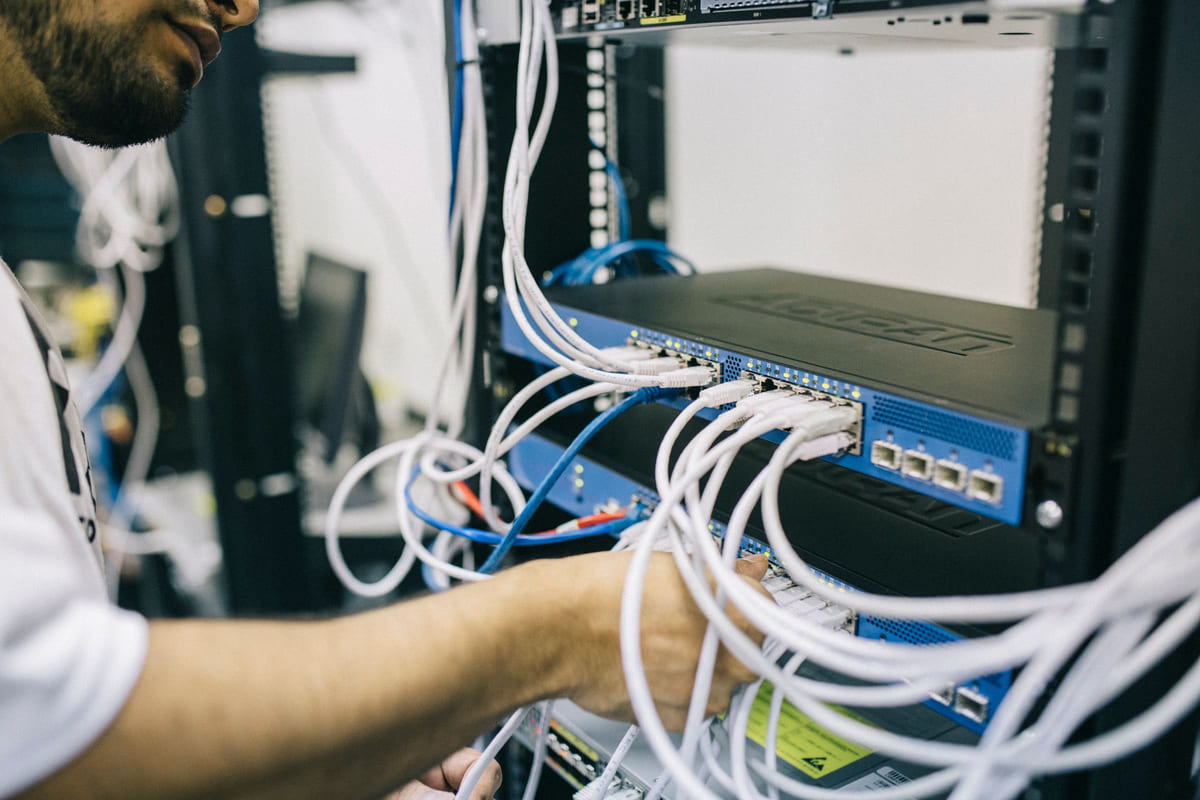 An IT technician working on network cables in a server rack.
