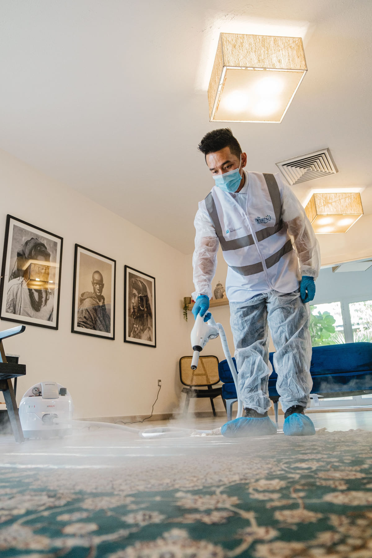 A worker using carpet-cleaning equipment in a furnished room.