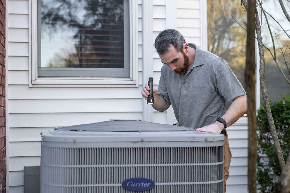 A technician inspecting an outdoor air-conditioning condenser beside a house.
