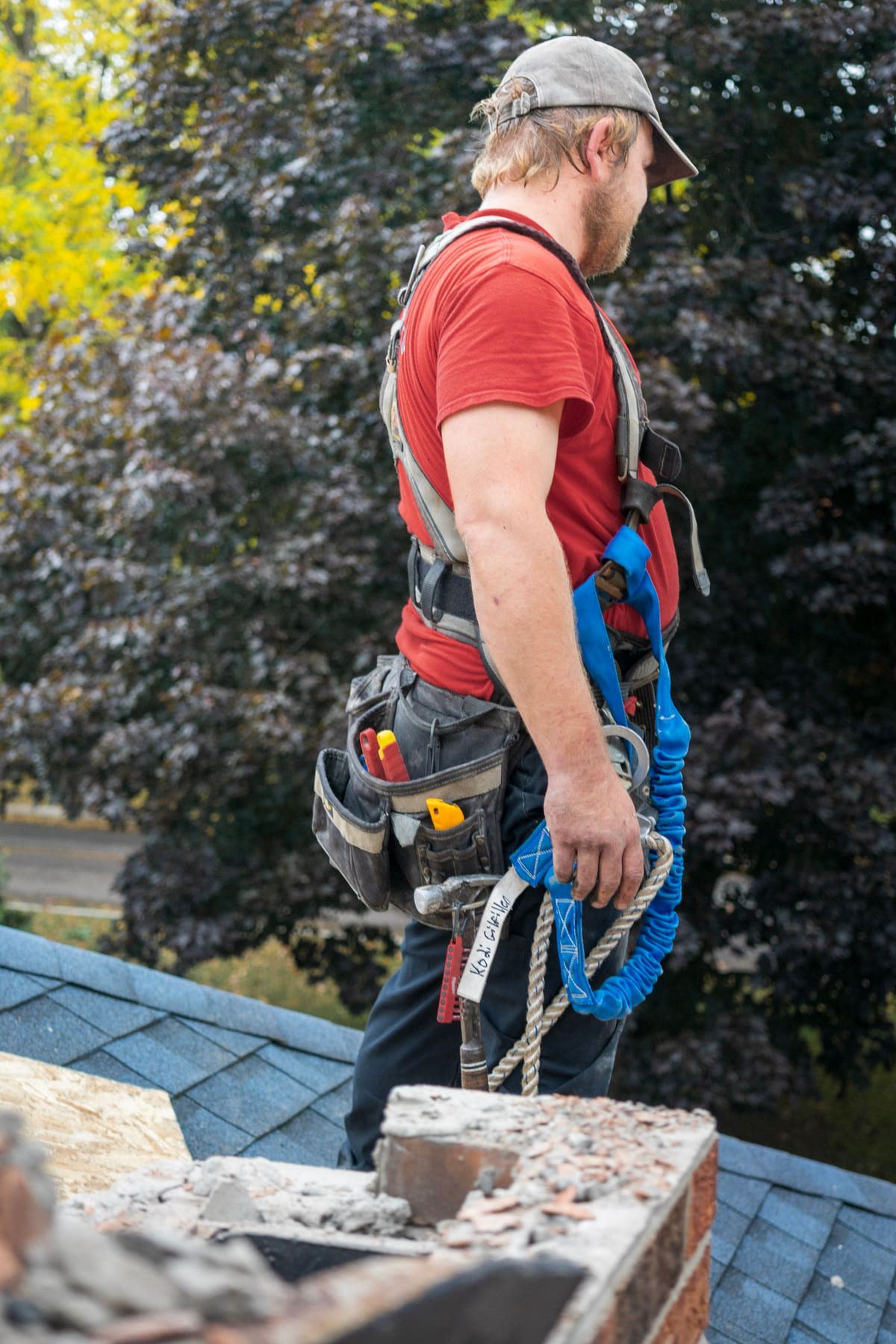 A worker wearing safety equipment standing beside a chimney on a roof.