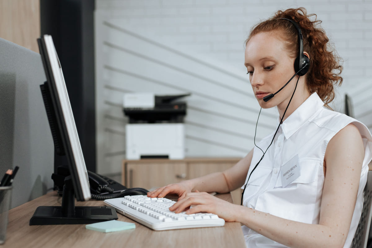 A customer-service worker typing at a computer while wearing a headset.