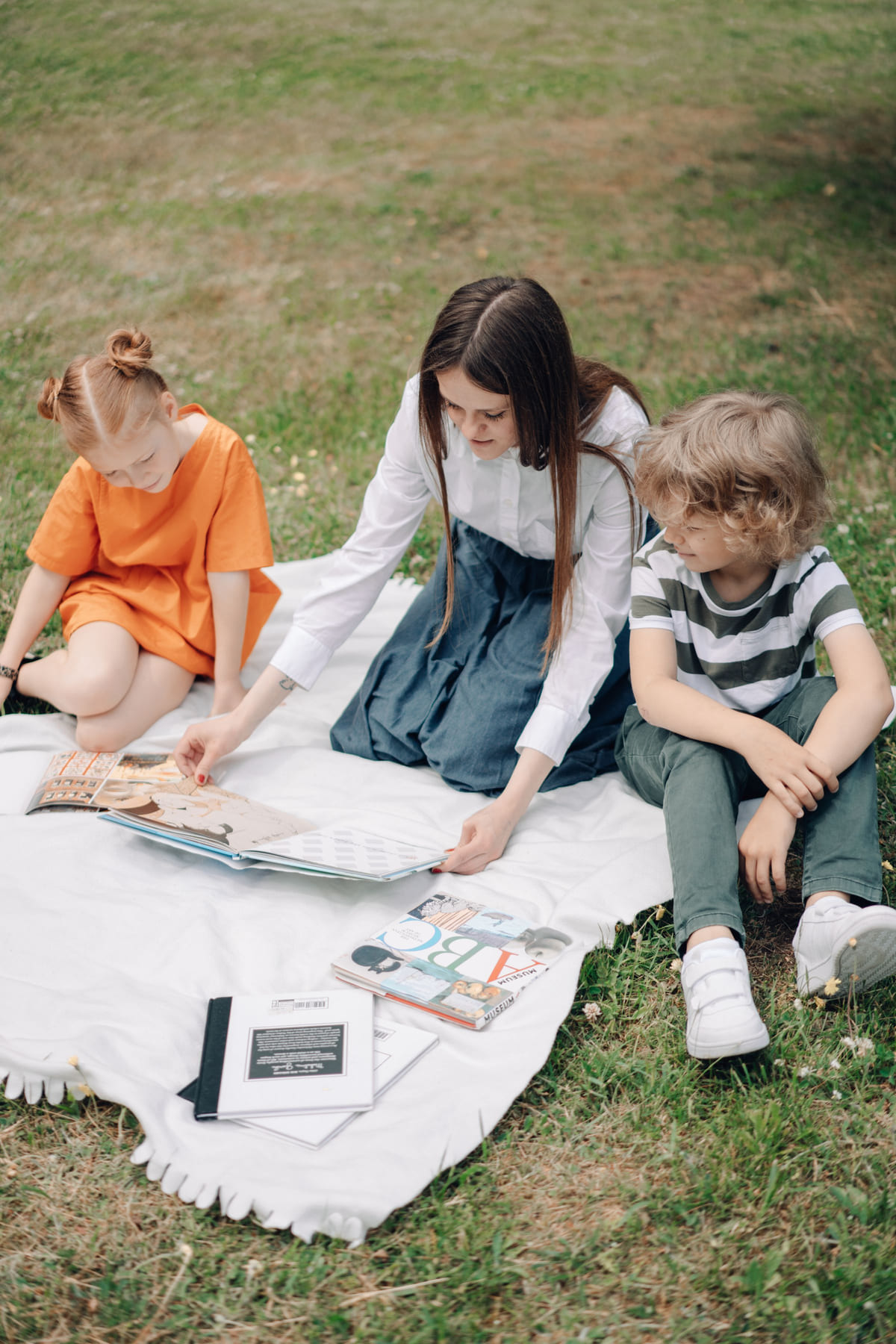 An adult leading a learning activity with children on a blanket outdoors.
