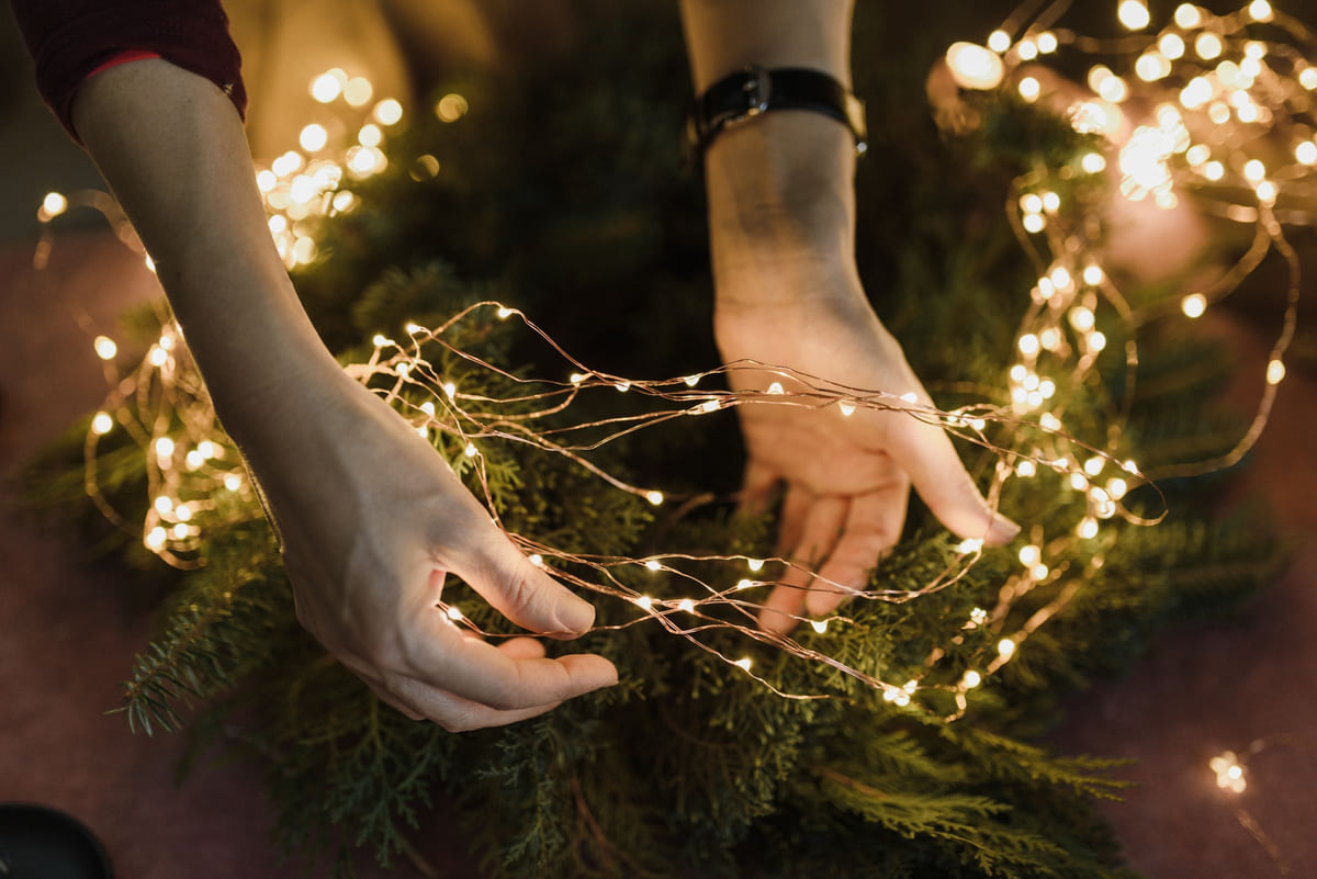 Hands arranging a strand of warm white Christmas lights.